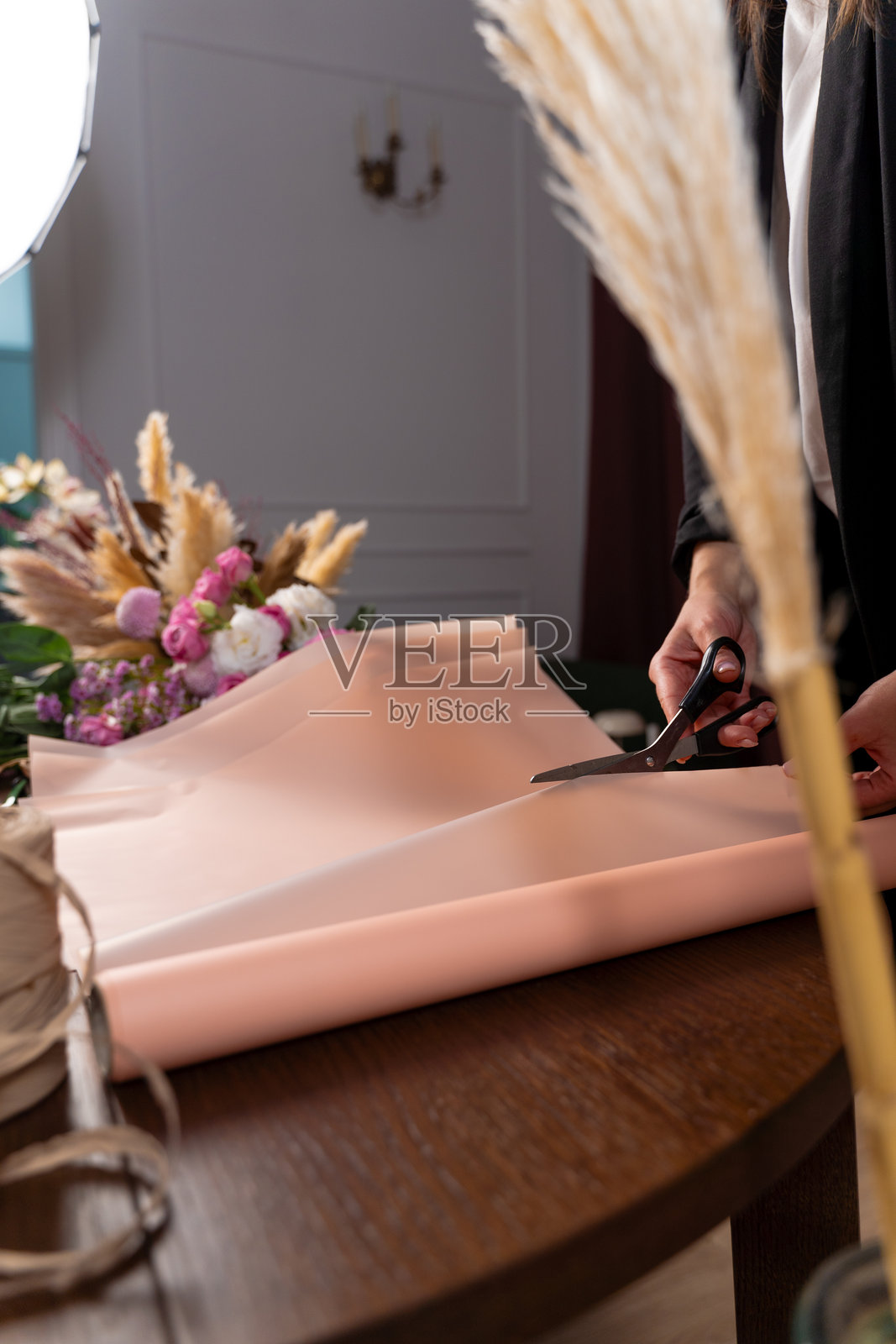 花店里的花艺师用包装纸包裹混合花束。花艺师为客户制作玫瑰和康乃馨的花卉组合。照片摄影图片