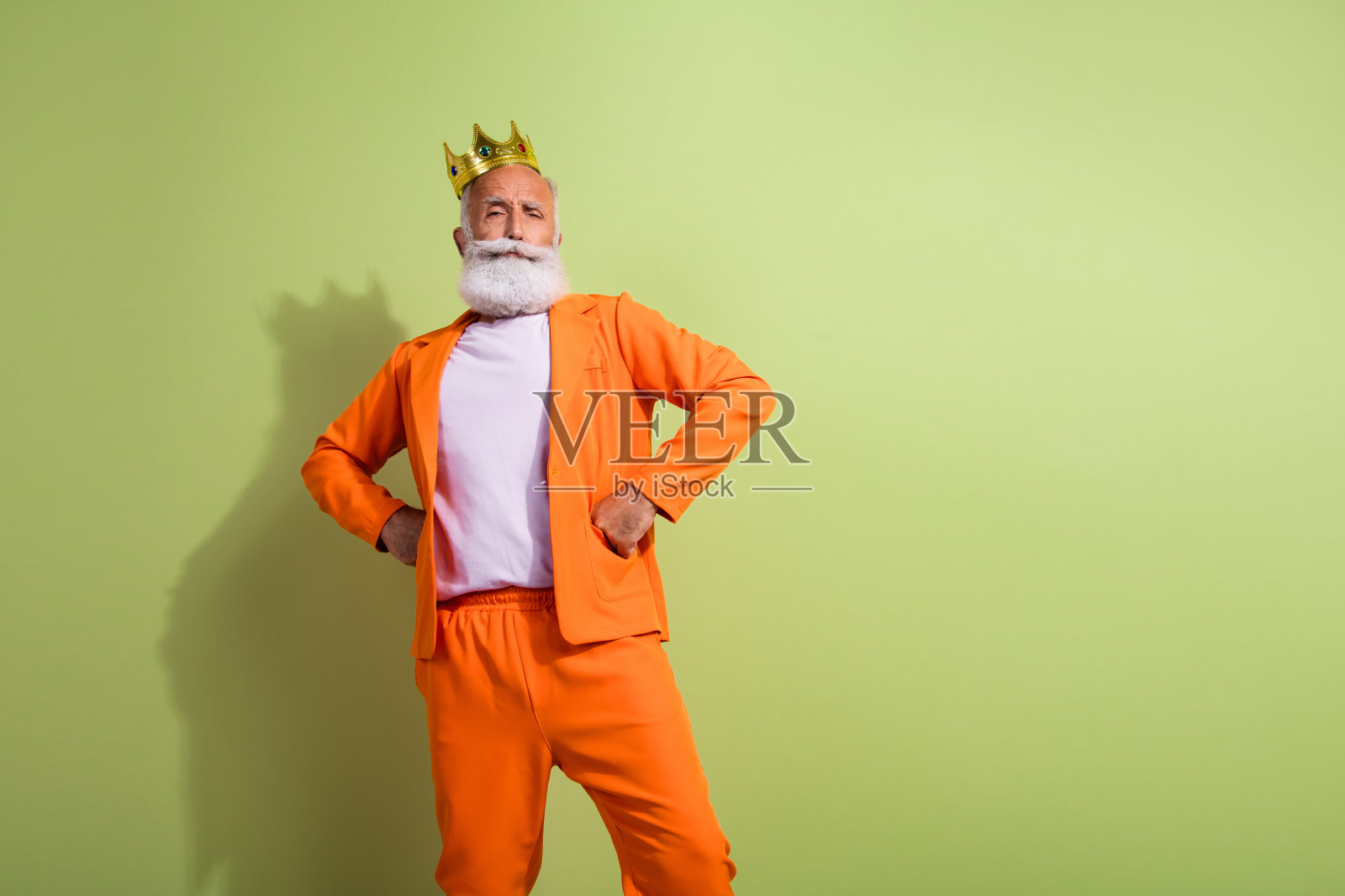 穿着橙色西装的古怪时尚祖父在绿色背景前摆姿势，留出空白空间。照片摄影图片