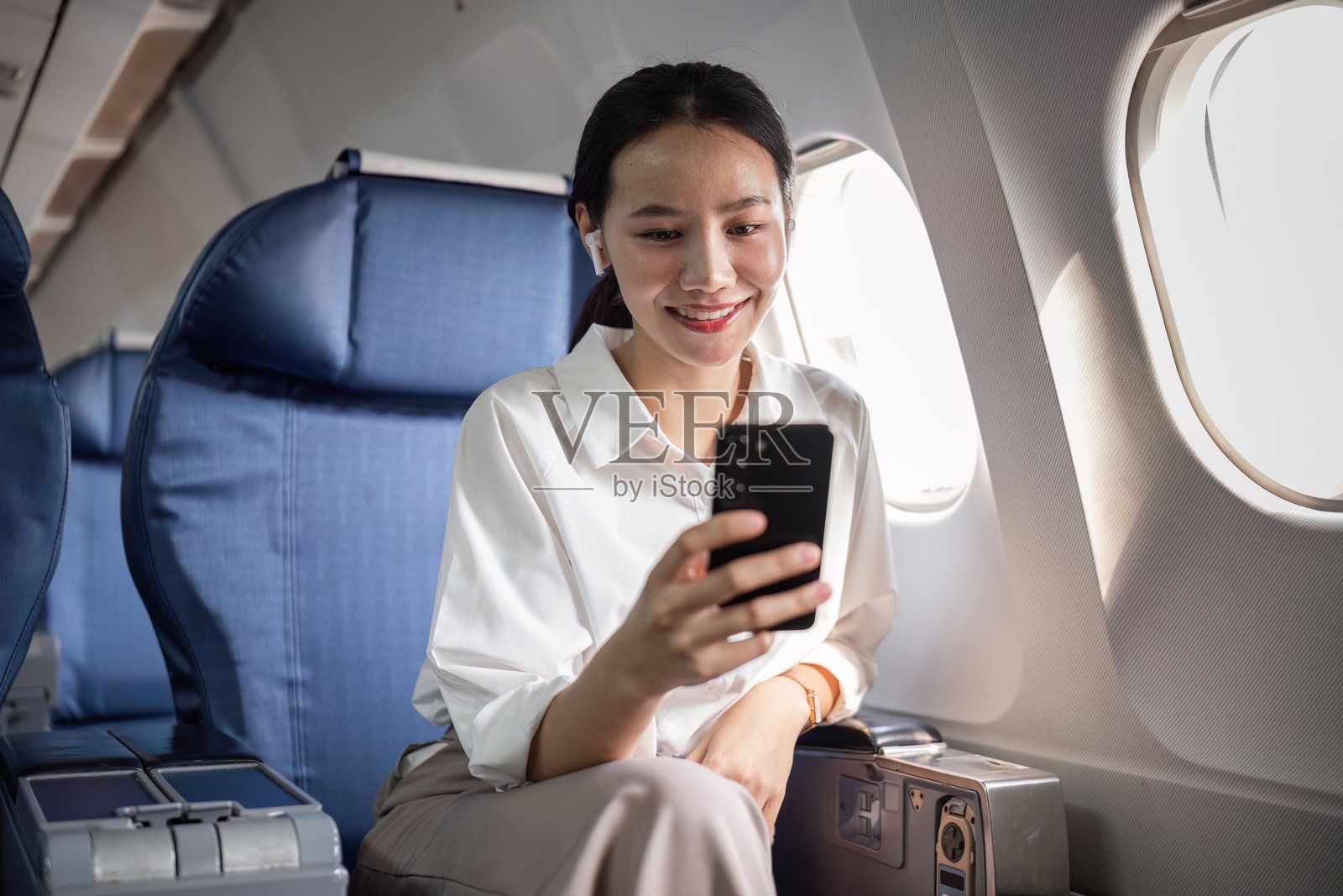 自信的女商人在飞机上旅行，使用智能手机远程工作，现代职业旅程，飞行中的高效工作照片摄影图片
