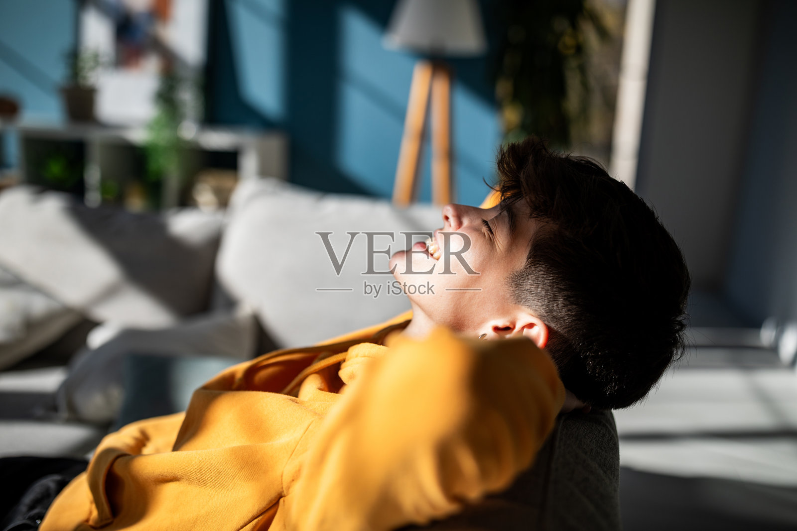 一个人在阳光下放松，坐在灰色沙发上。照片摄影图片