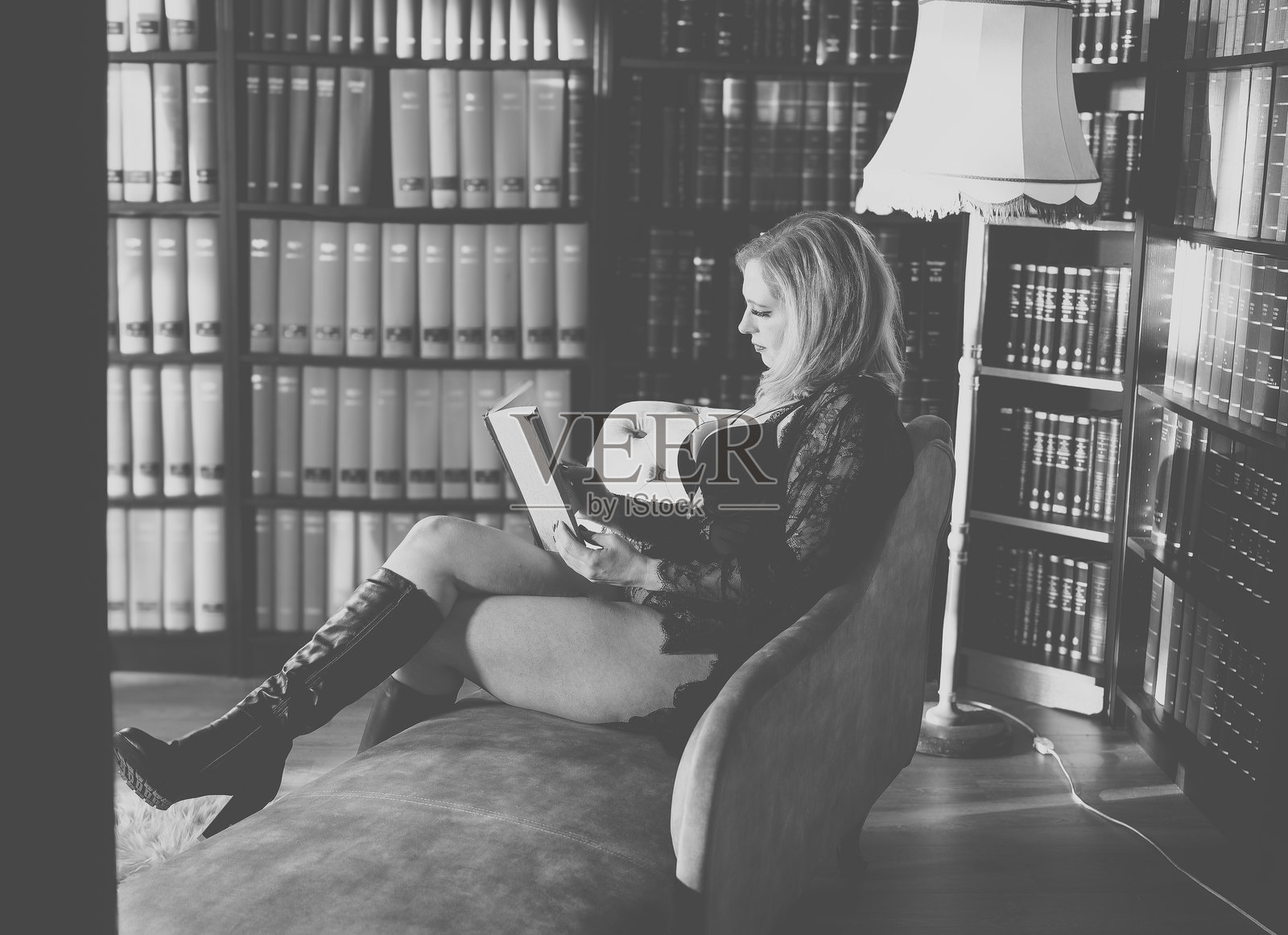 女人在温馨的图书馆环境中阅读一本书，傍晚时分灯光柔和。照片摄影图片