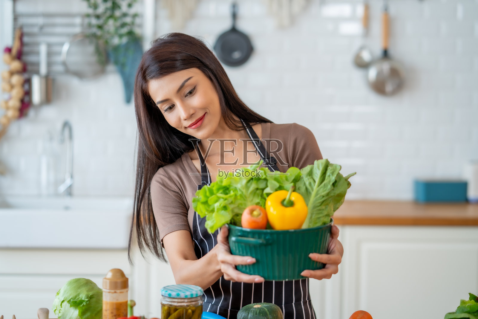 女人在厨房里手持盛有新鲜蔬菜的碗，正在准备健康的餐点。场景传达出快乐和健康的感觉。照片摄影图片