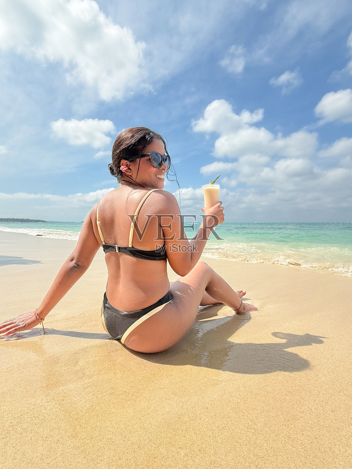 年轻女性在热带海滩上放松，手持鸡尾酒，享受夏季假期照片摄影图片