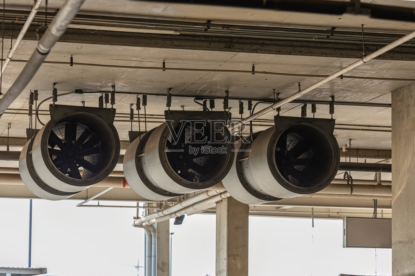 现代建筑内的风扇。停车场通风系统。鼓风机为工厂的密闭空间提供空气流动。工业风扇加热器和冷却器。照片摄影图片