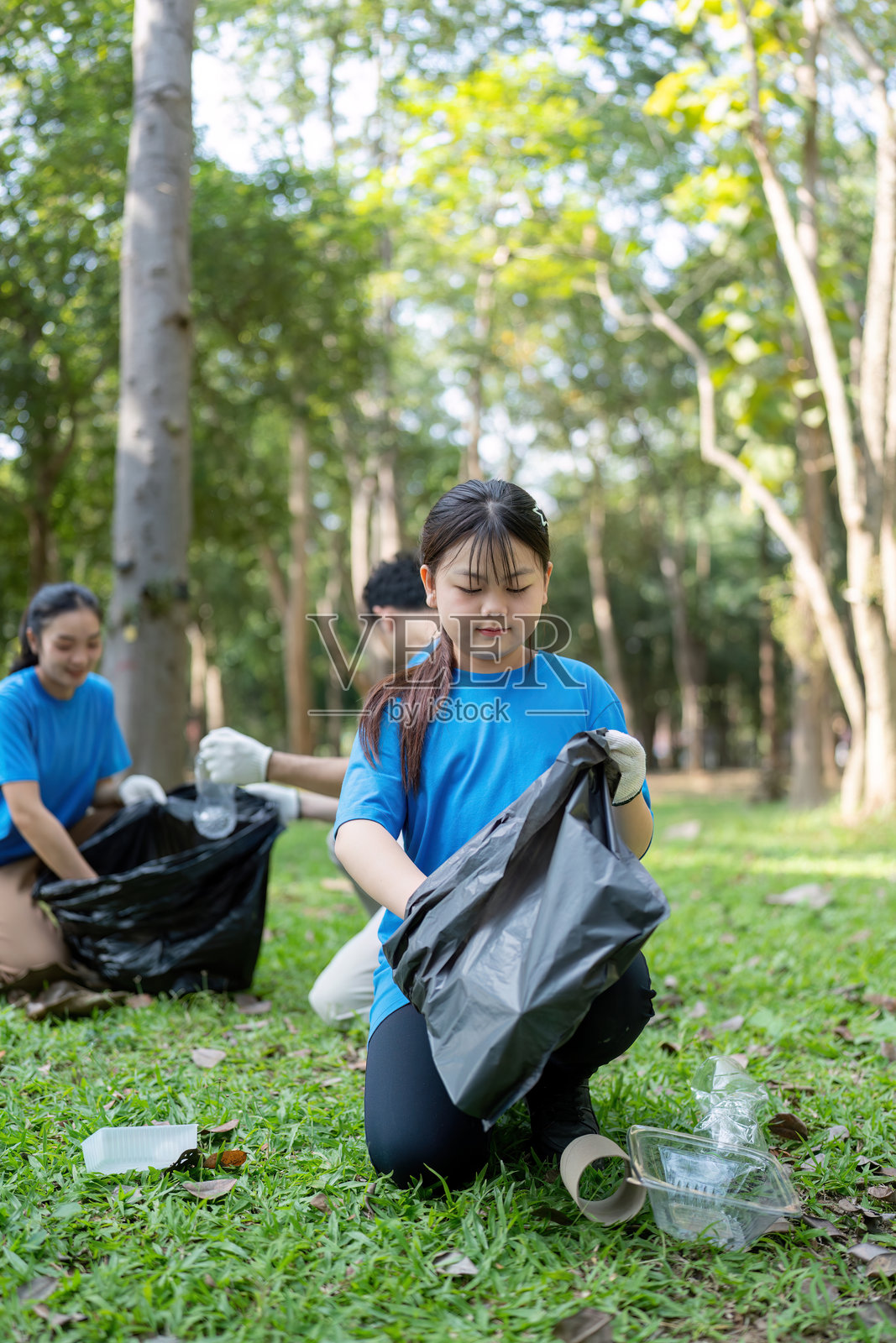 家庭志愿者在自然公园收集垃圾，进行环境清理工作，风景如画的绿色景观，社区参与。照片摄影图片