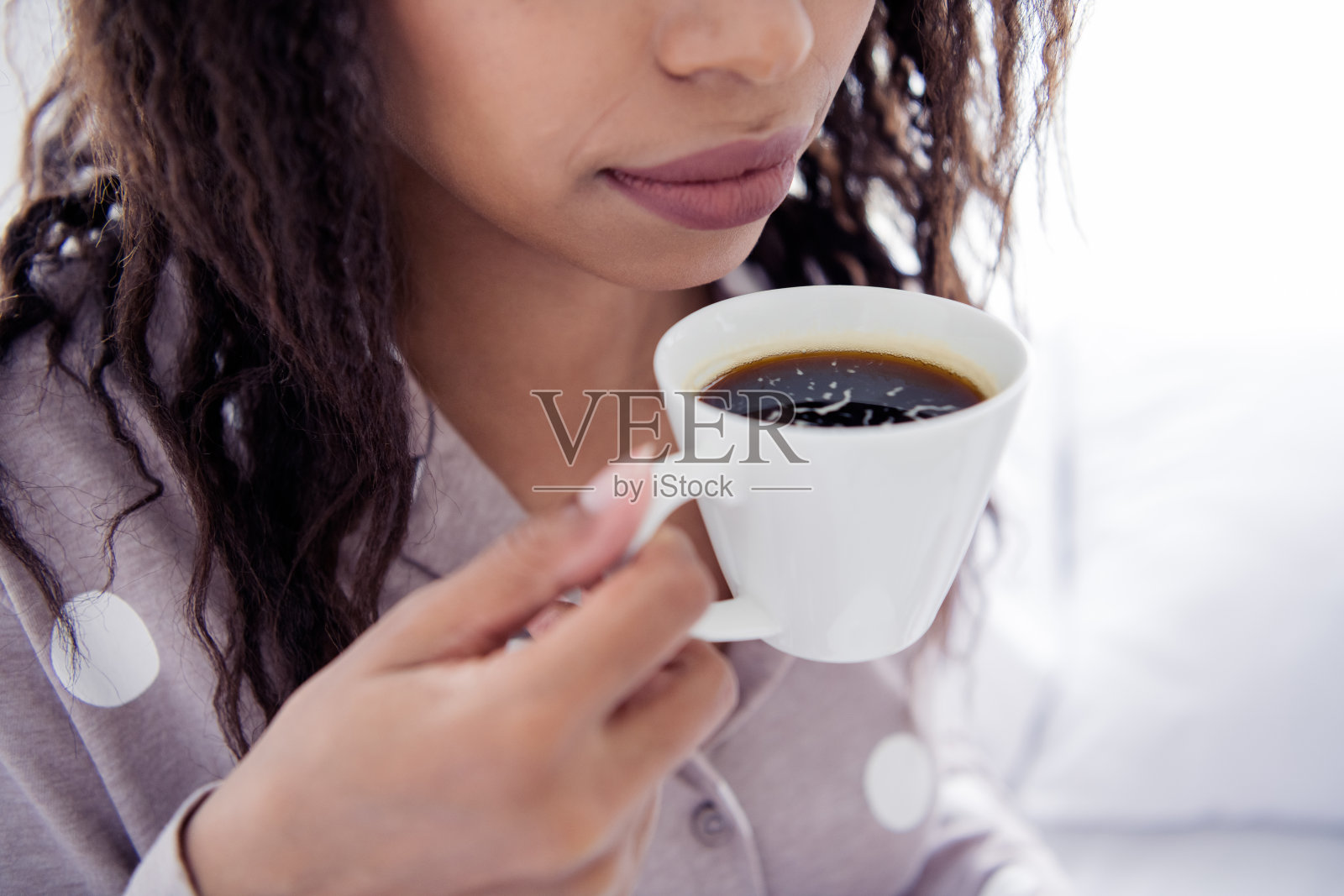 年轻女性穿着舒适的睡衣，在自然光照下享受床上的早晨咖啡照片摄影图片