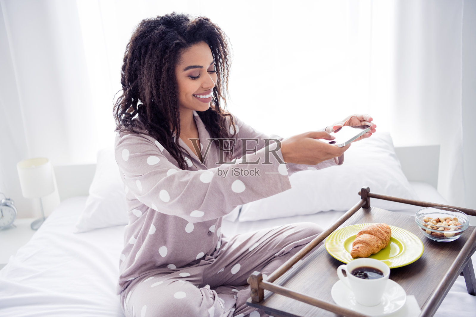 年轻女性穿着波点睡衣，在舒适的卧室里享受早晨的咖啡和可颂面包照片摄影图片