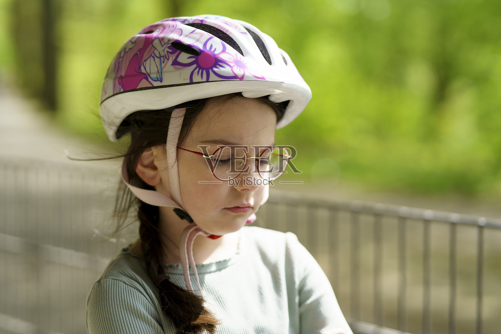 戴着眼镜和头盔的小女孩骑自行车，显得有些伤心。活泼孩子的伤感概念。照片摄影图片