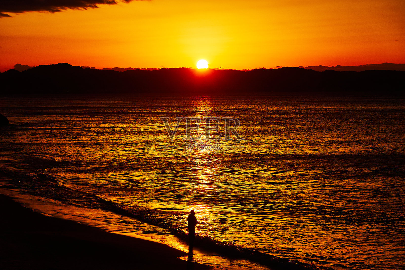 日出时分，海滩的壮丽景色，剪影般的人们在戏剧性的天空下伫立。照片摄影图片