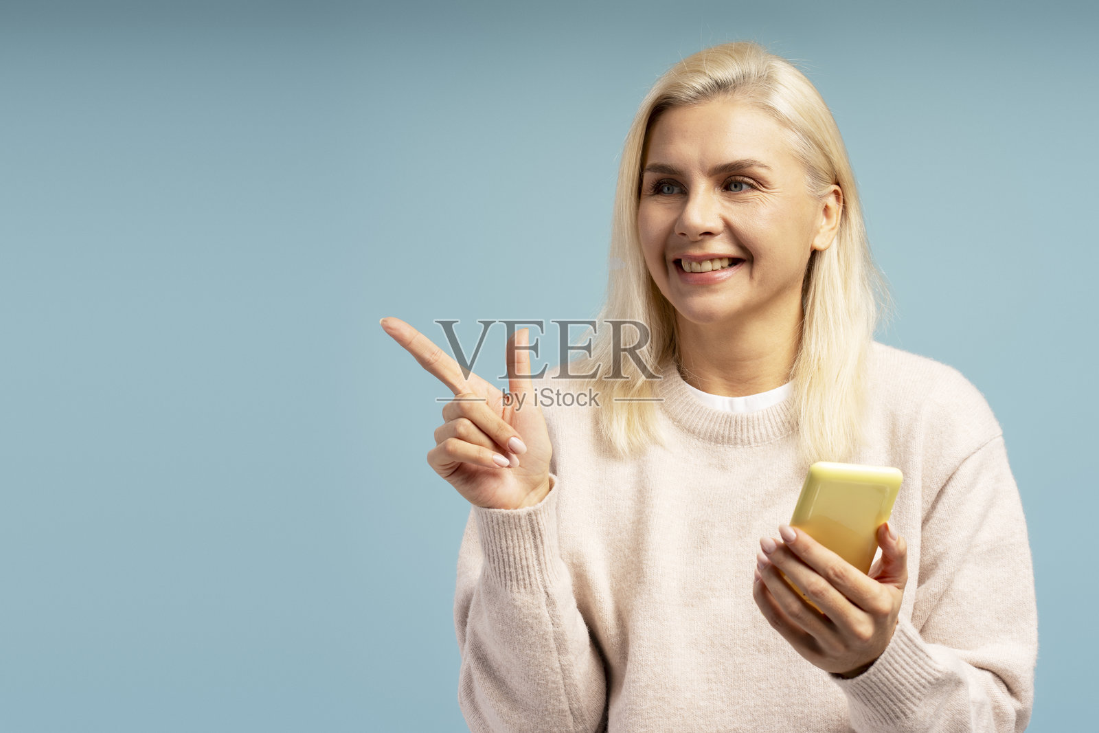 微笑的女性在蓝色背景下指着手指并拿着智能手机照片摄影图片