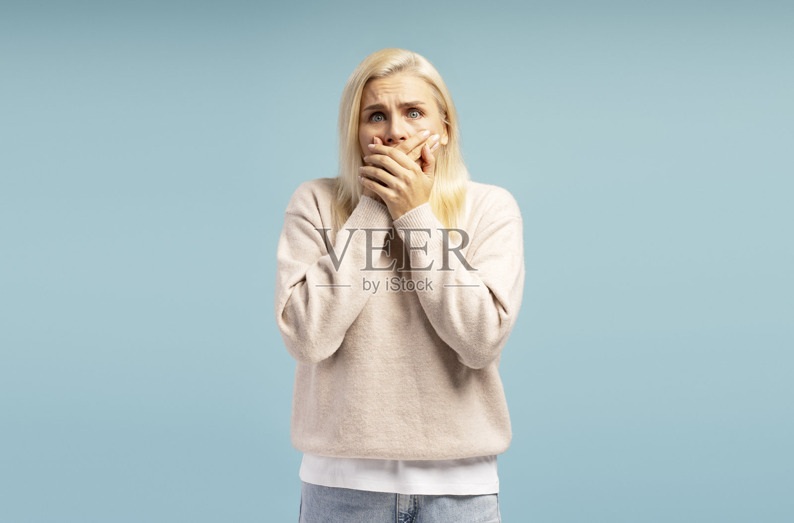震惊的女人用手捂住嘴巴，背景为蓝色照片摄影图片