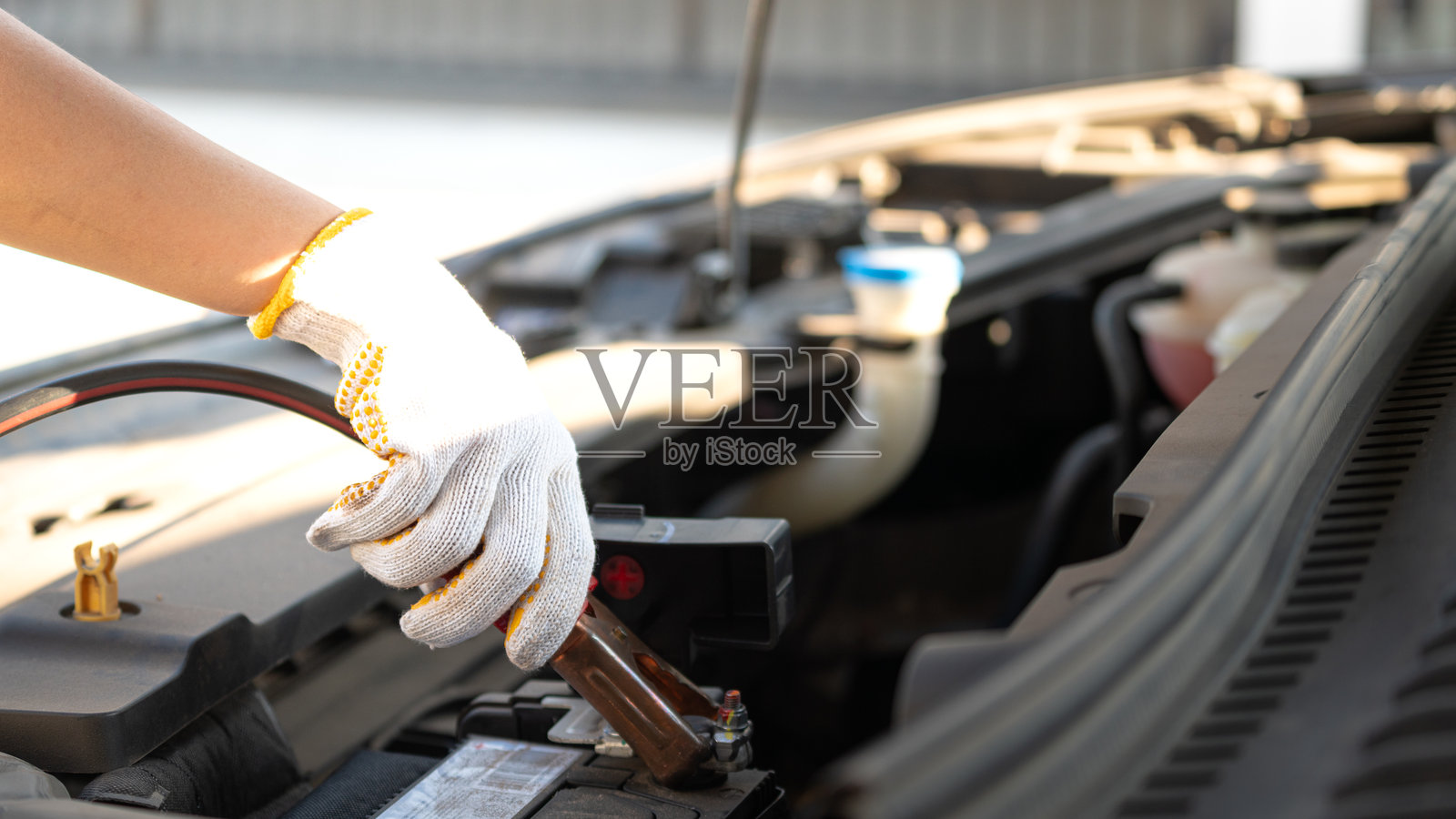 技术人员的手正在使用紧急夹具套件夹住12V汽车电池的正极以进行搭电。照片摄影图片