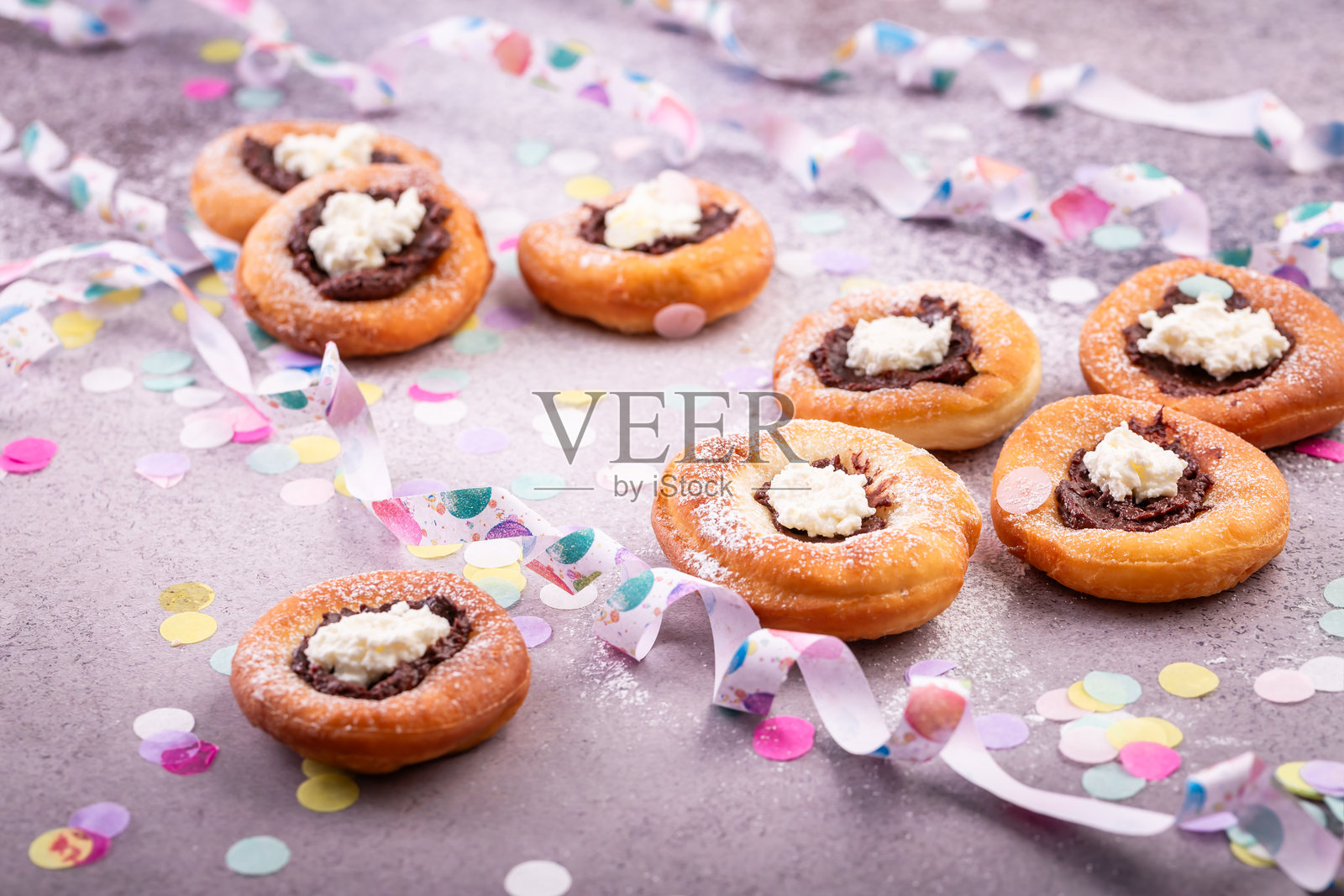 嘉年华糖粉炸面圈，夹有果酱和奶油奶酪，纸质彩带和五彩纸屑照片摄影图片