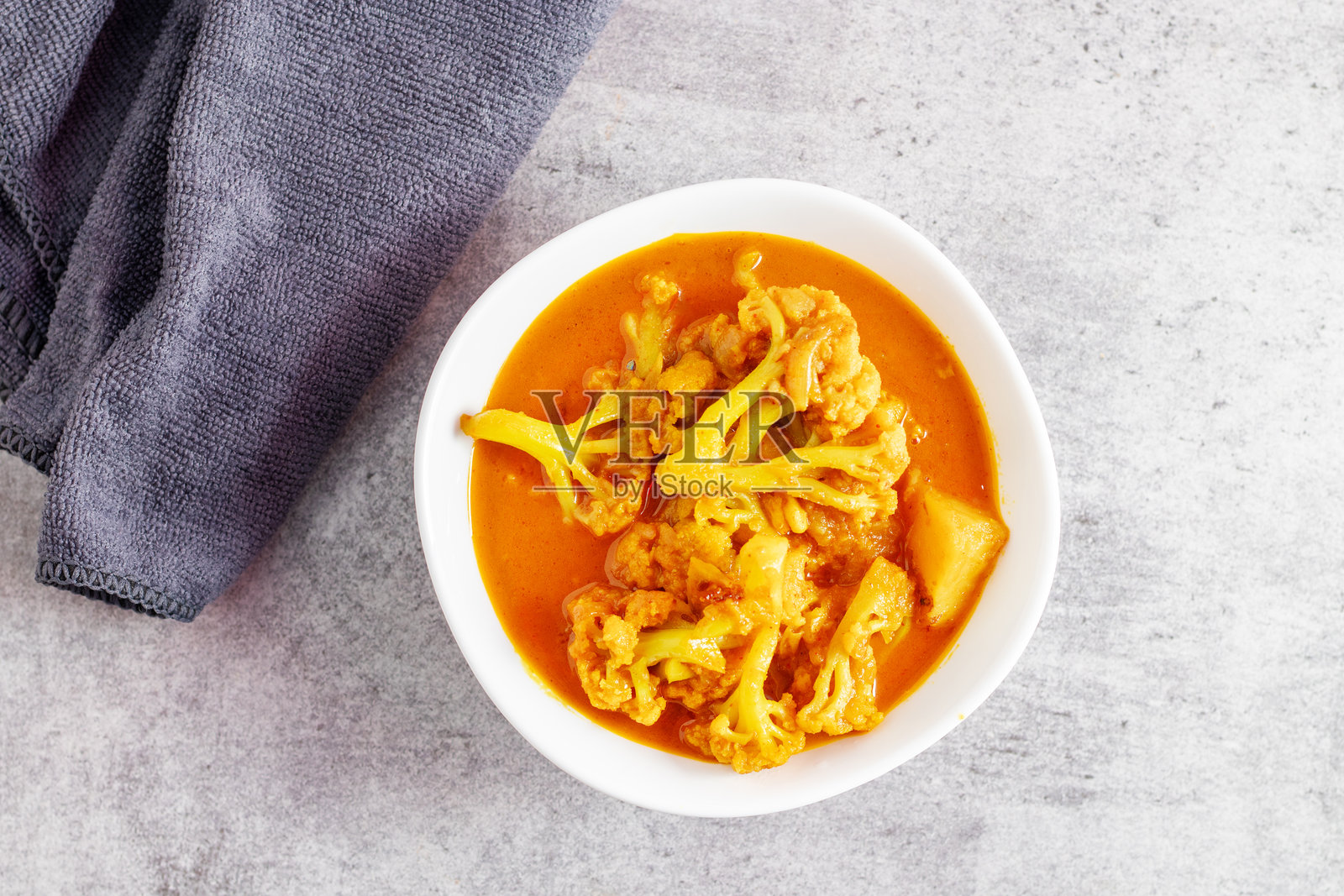 一碗色彩鲜艳的黄色咖喱，包含花椰菜和土豆，盛放在传统印度风格的铜盘中。照片摄影图片