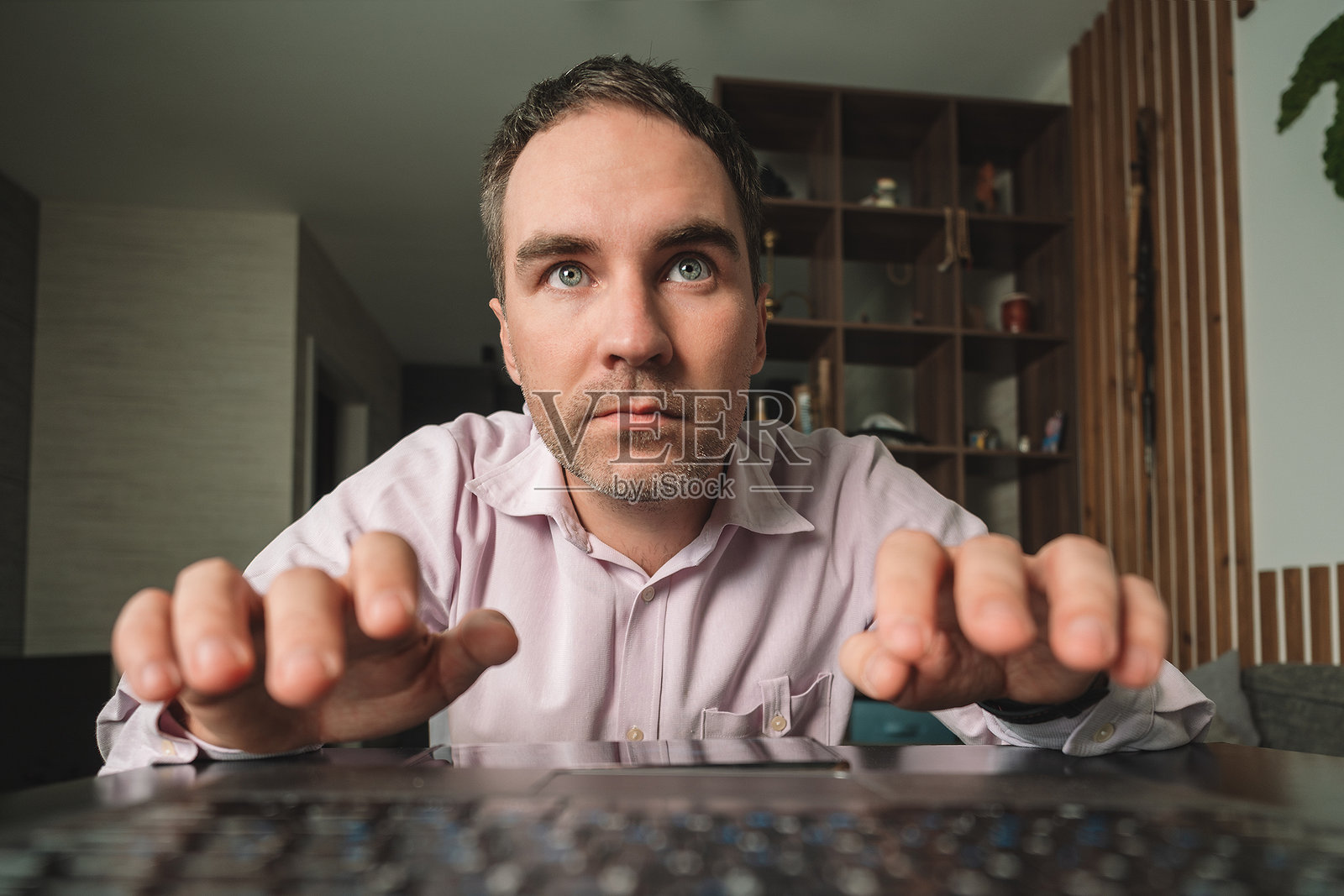 戴眼镜的男子手持笔记本电脑，面露极度困惑，背景为家居环境。照片摄影图片