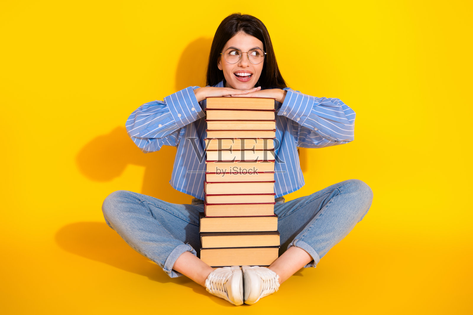 年轻女性在鲜艳的黄色背景前，面带快乐的表情，手中捧着一叠书籍照片摄影图片