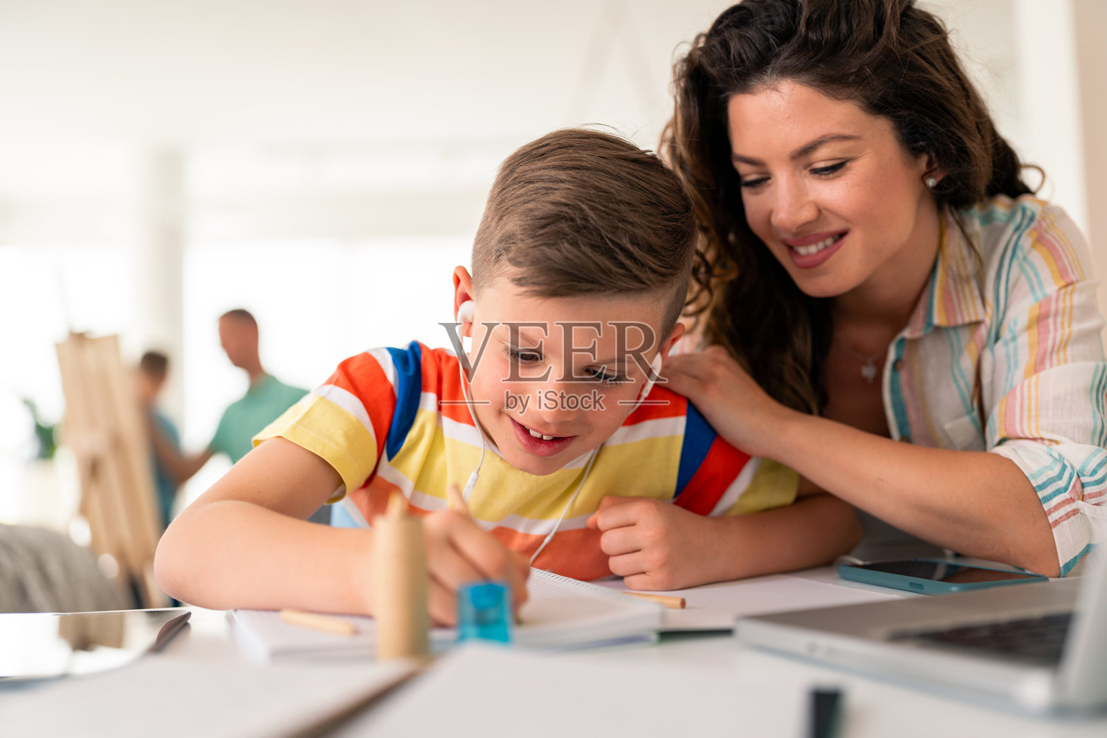 支持的母亲在家里的桌子上帮助年轻学生完成作业照片摄影图片