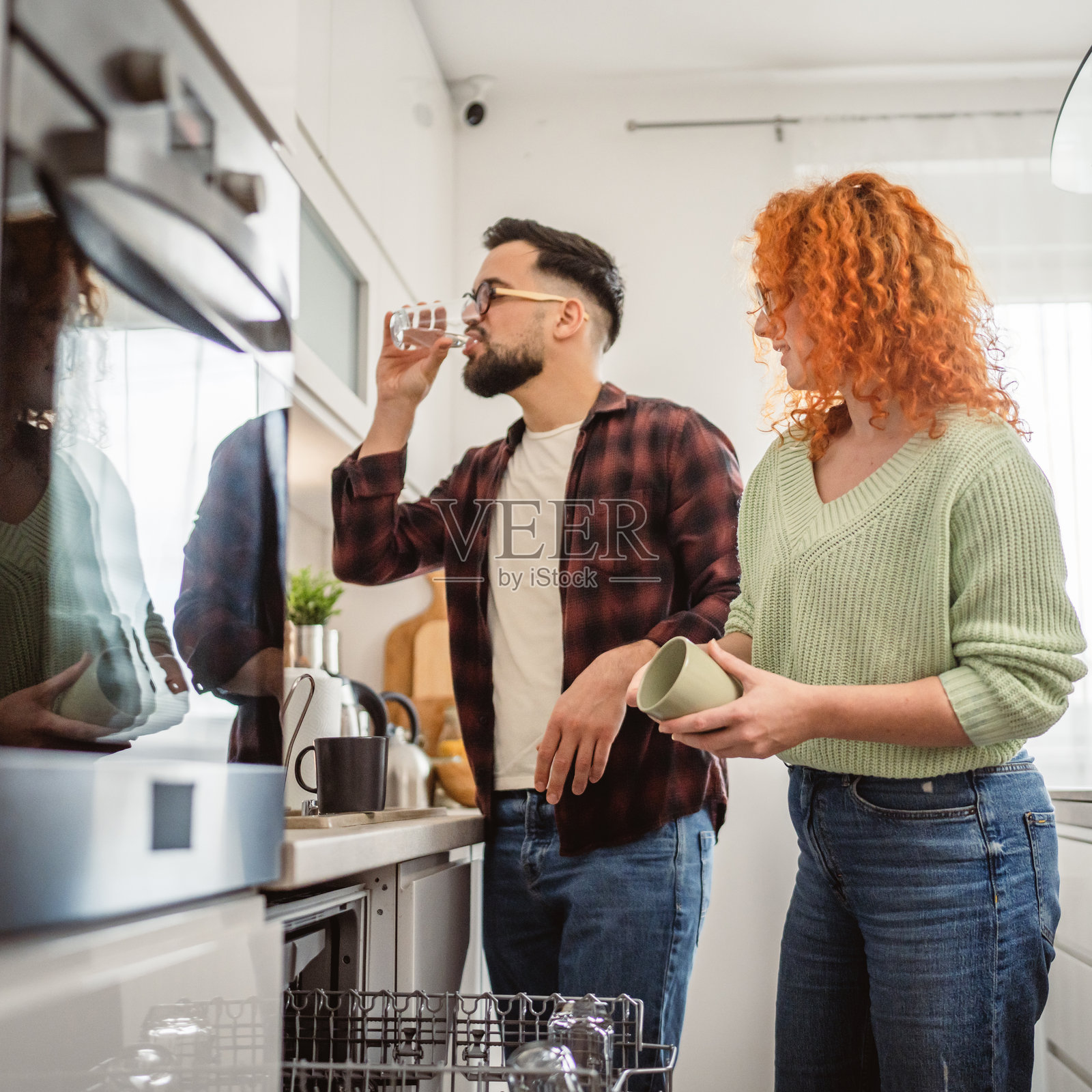 男朋友帮助女朋友把碗碟放进厨房的洗碗机里照片摄影图片