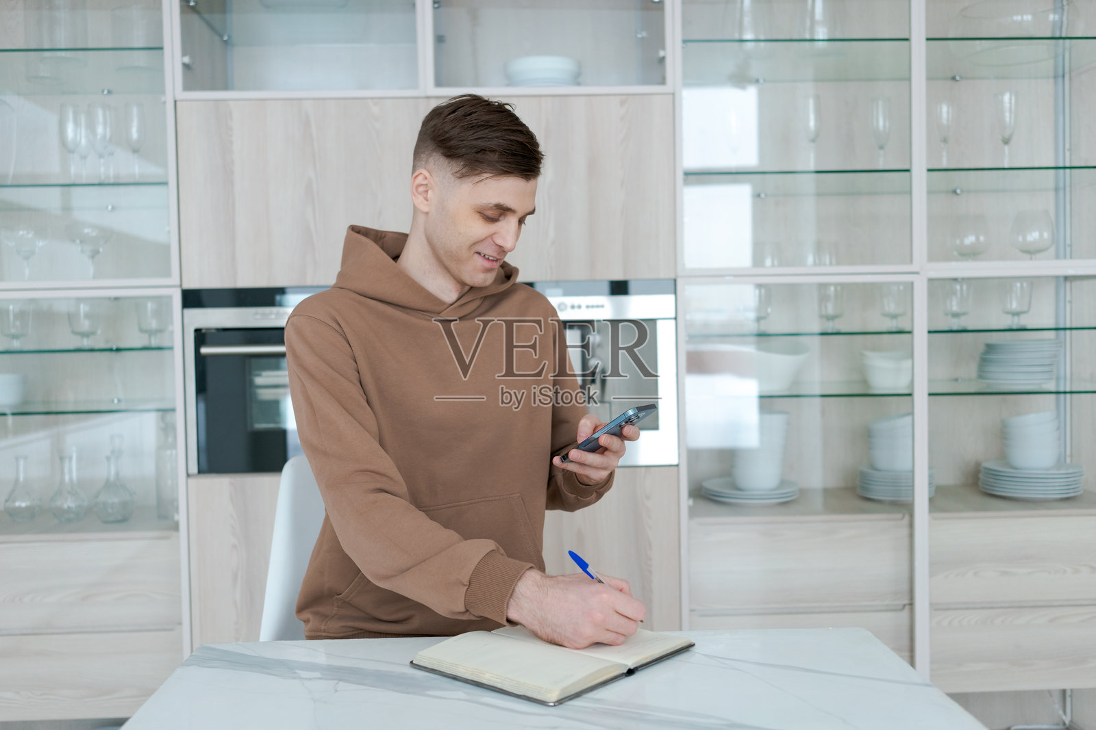 男子坐在桌子旁，手边有一本笔记本和一部手机。照片摄影图片