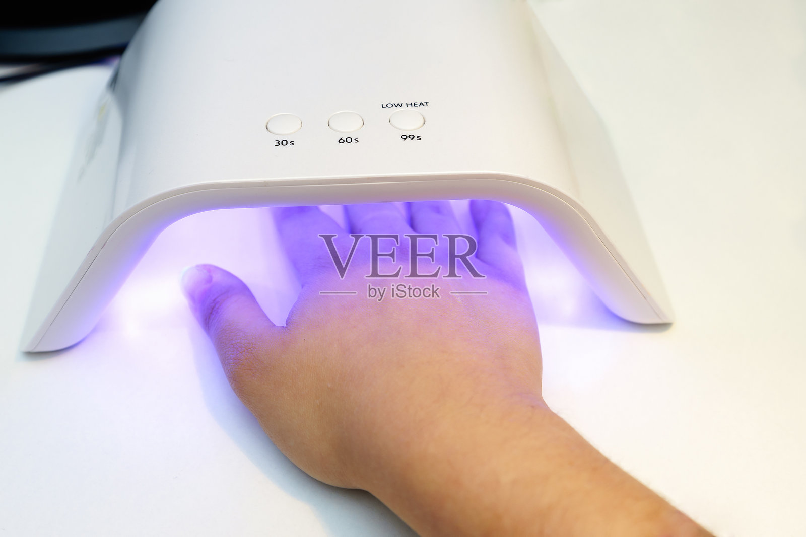 在白色表面上，手放在紫外线LED指甲灯下固化凝胶指甲油照片摄影图片