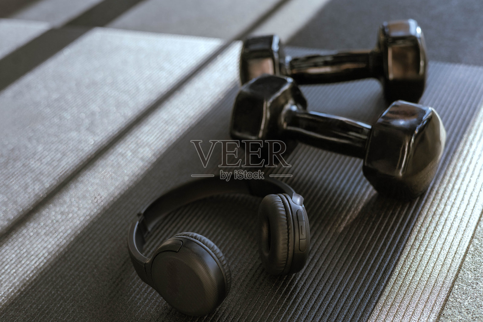 黑色哑铃和音响耳机放在健身房时尚的瑜伽垫上。照片摄影图片