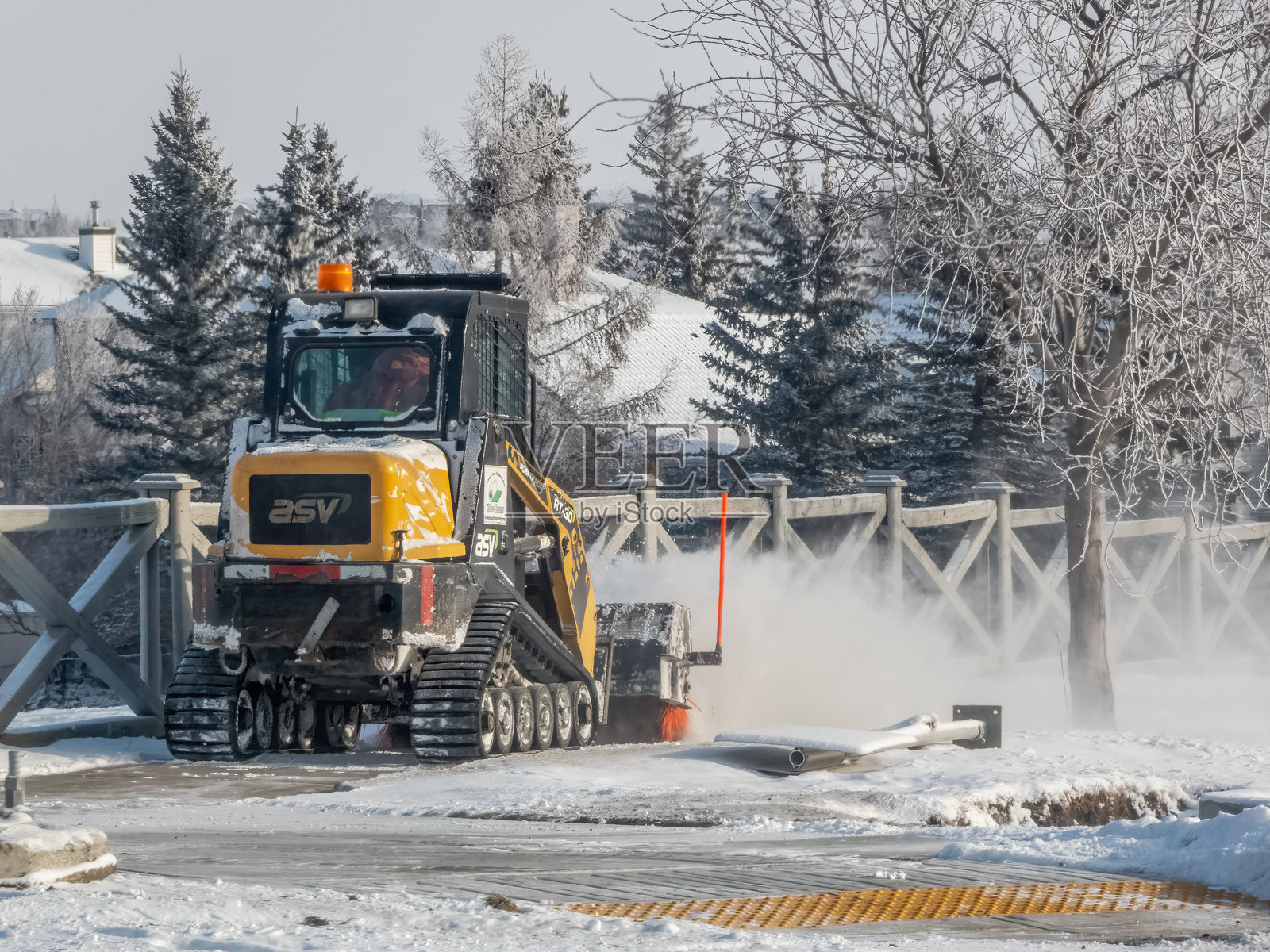 一台黄色的ASV RT-30紧凑型履带装载机正在清理小路上的积雪，强大的履带和高效的设计应对冬季的挑战。雪花在空中飞舞。照片摄影图片
