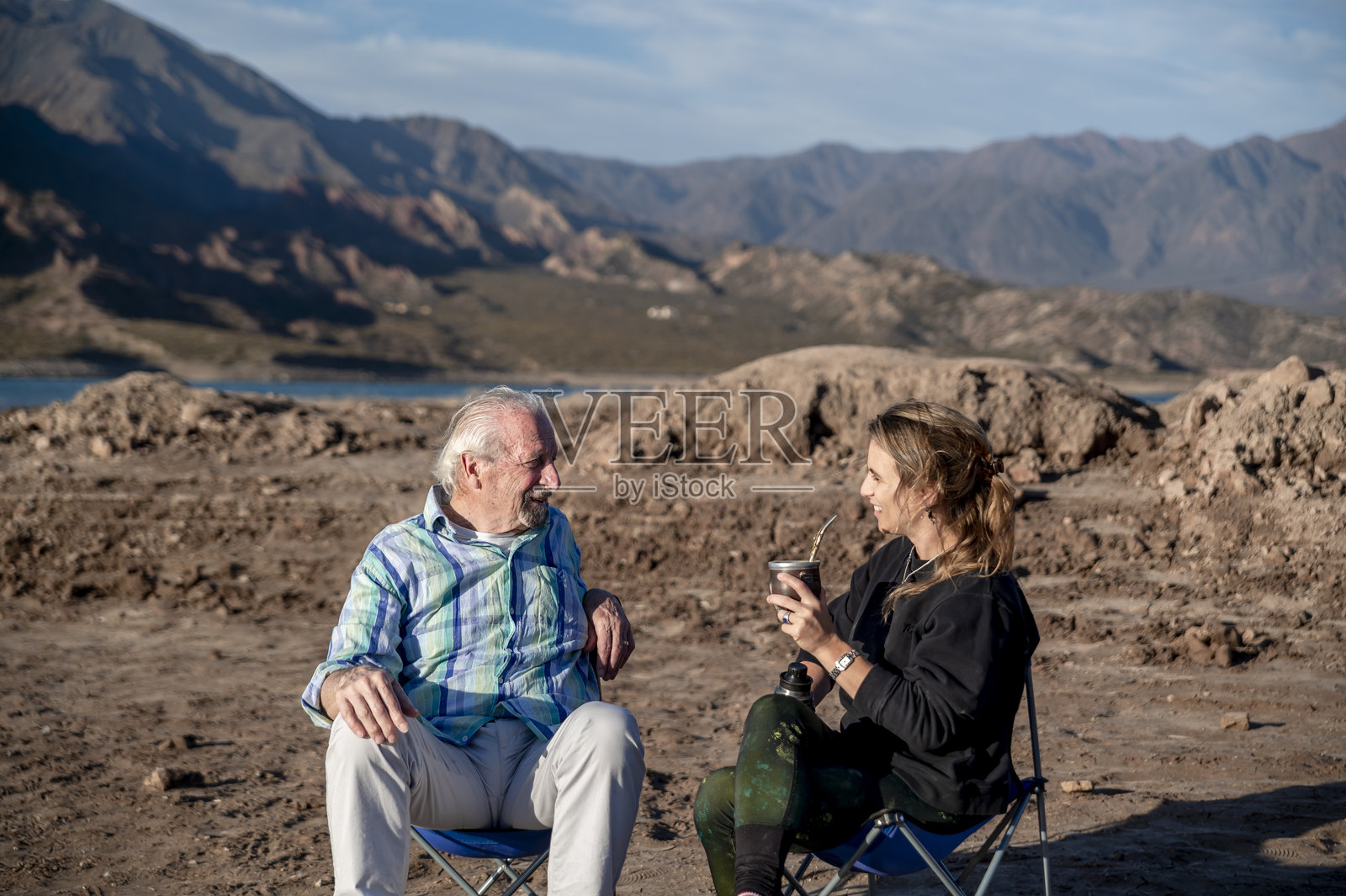 女人和她的祖父坐在户外的露营椅上交谈，享受大自然。照片摄影图片