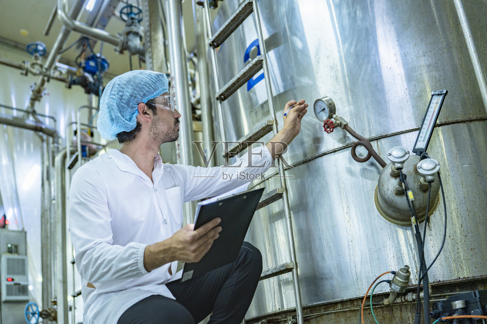 专业人员在制造设施中对不锈钢罐进行质量检查，强调效率、工业创新以及对安全和标准的承诺。照片摄影图片