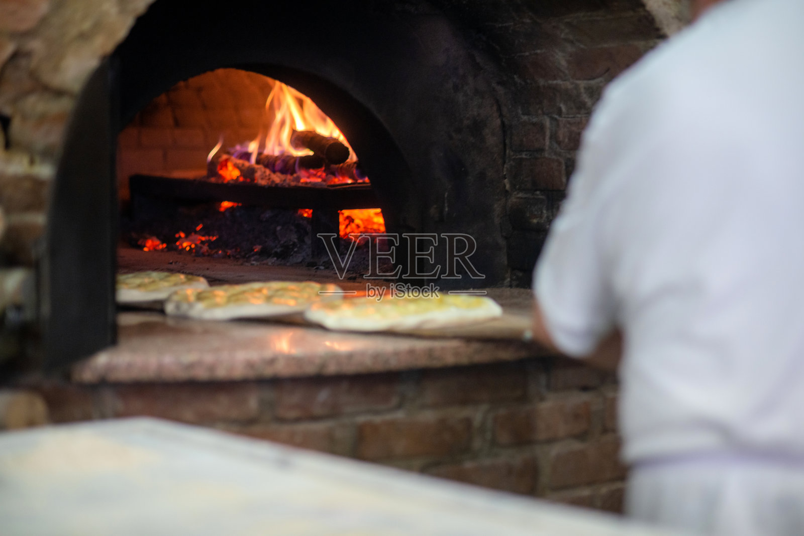 老面包师傅在土耳其伊斯坦布尔的一家烤肉餐厅用面包铲将一种传统的土耳其皮塔饼（称为“trnak pide”）放入木火烤炉中。照片摄影图片