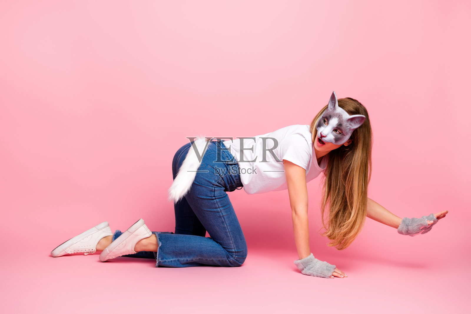 年轻女性穿着休闲的猫主题服装，在粉色背景前俏皮地摆姿势，四方女孩照片摄影图片