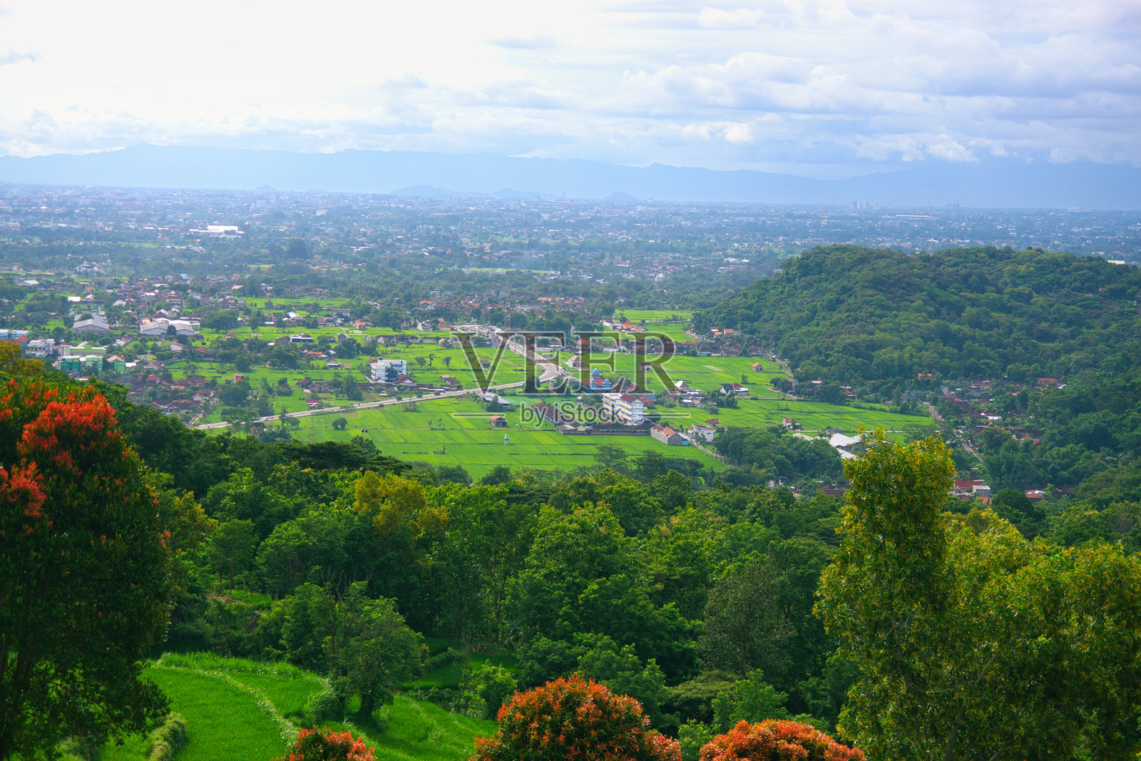 从日惹的特宾布雷克西拍摄的被郁郁葱葱的绿树和起伏山丘环绕的乡村村庄美景照片摄影图片