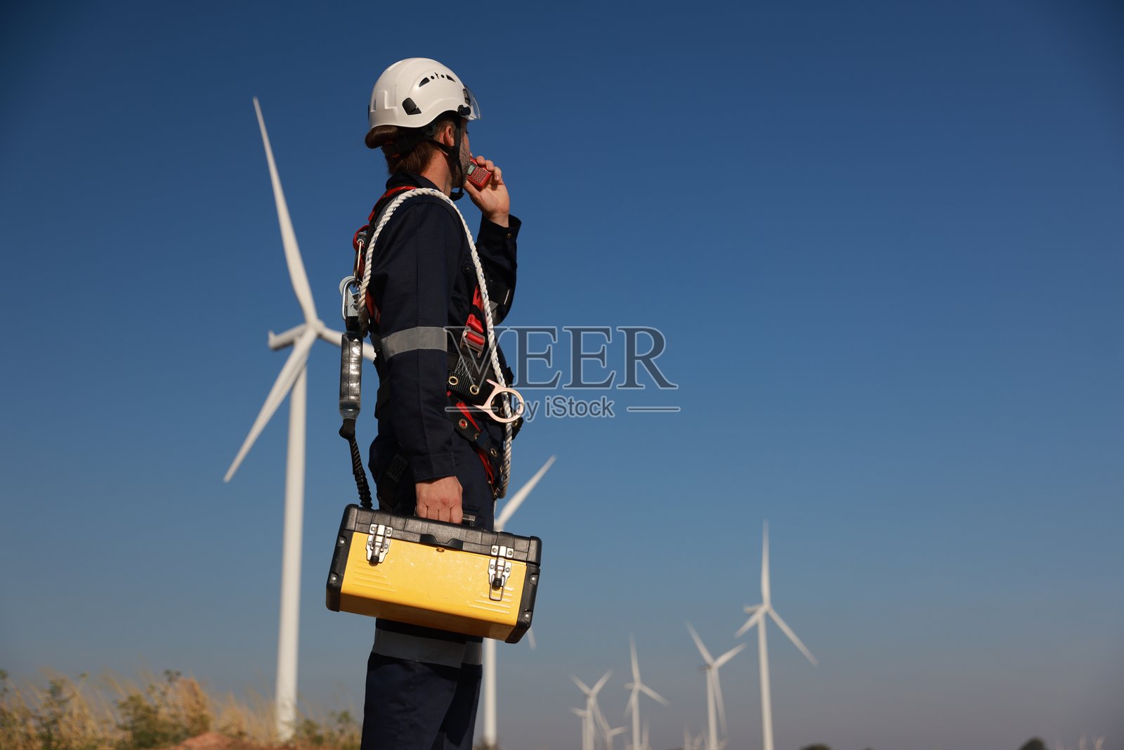一名穿着制服的男性维修技术员使用对讲机在风力发电站工作。碳中和与清洁能源。照片摄影图片