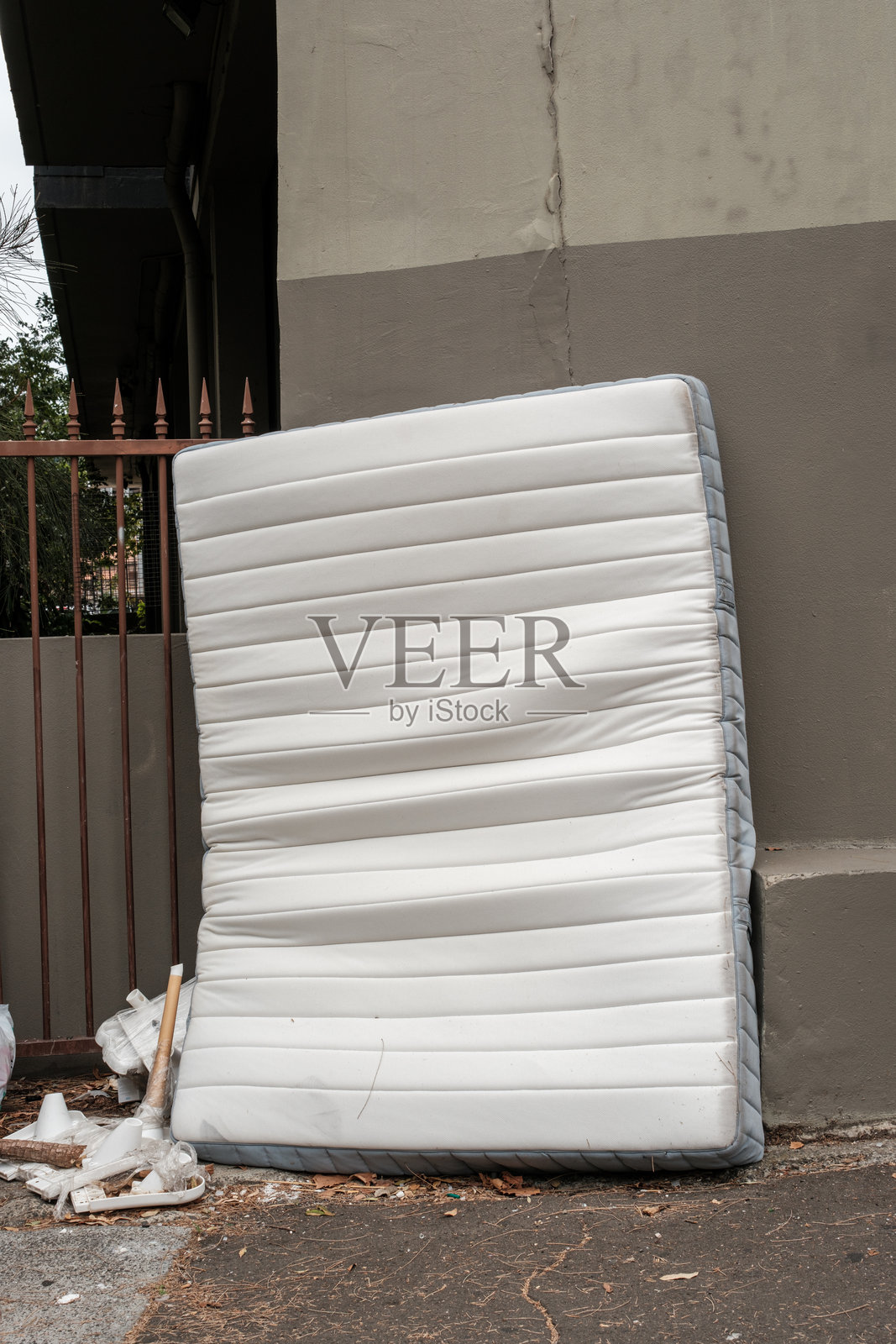人行道上靠墙丢弃的旧床垫。照片摄影图片