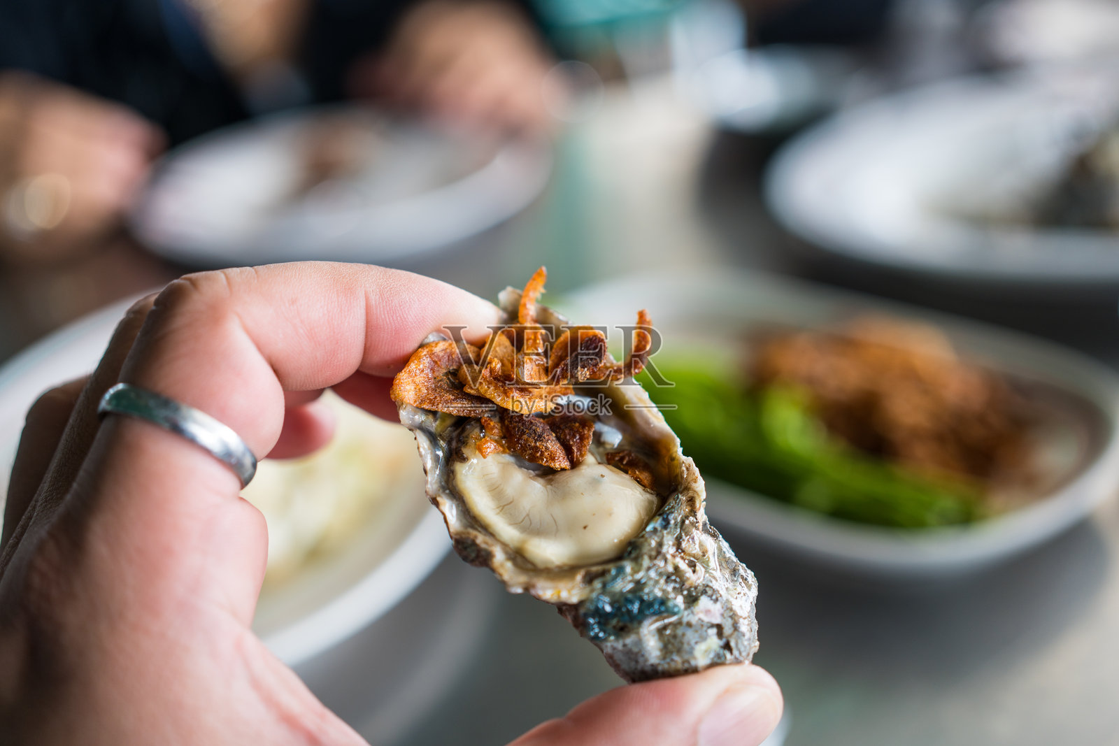 手中盛着新鲜生蚝，顶部撒有炸葱。照片摄影图片