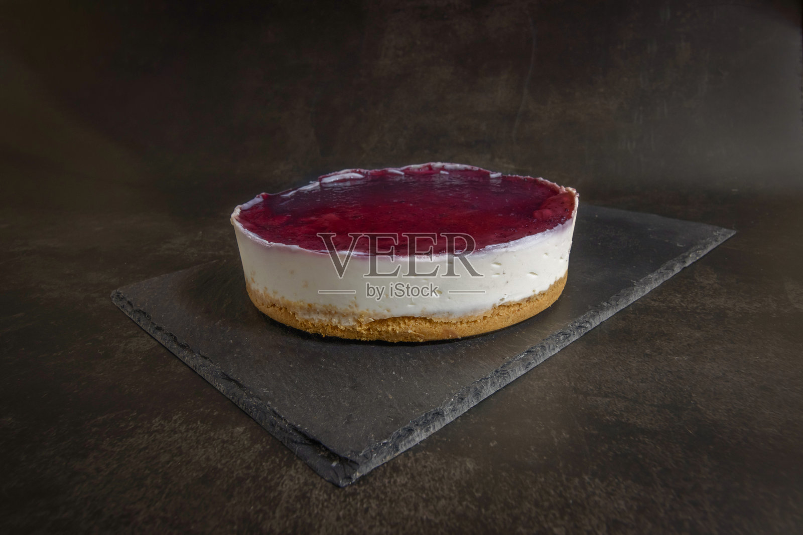 美味的蓝莓芝士蛋糕，配有松脆的饼干底、奶油般的馅料和光滑的浆果顶层，优雅地摆放在深色石板上。照片摄影图片