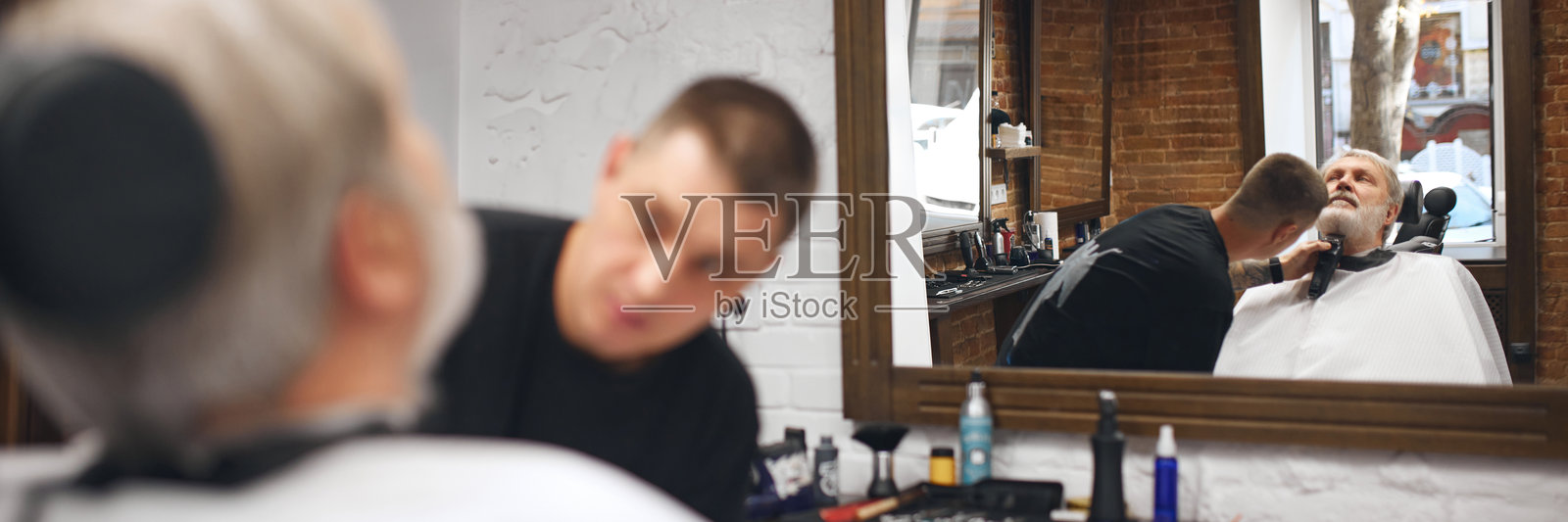 专注的理发师正在用电动修剪器修剪客户下巴的底部。老年人正在理发店理发。照片摄影图片