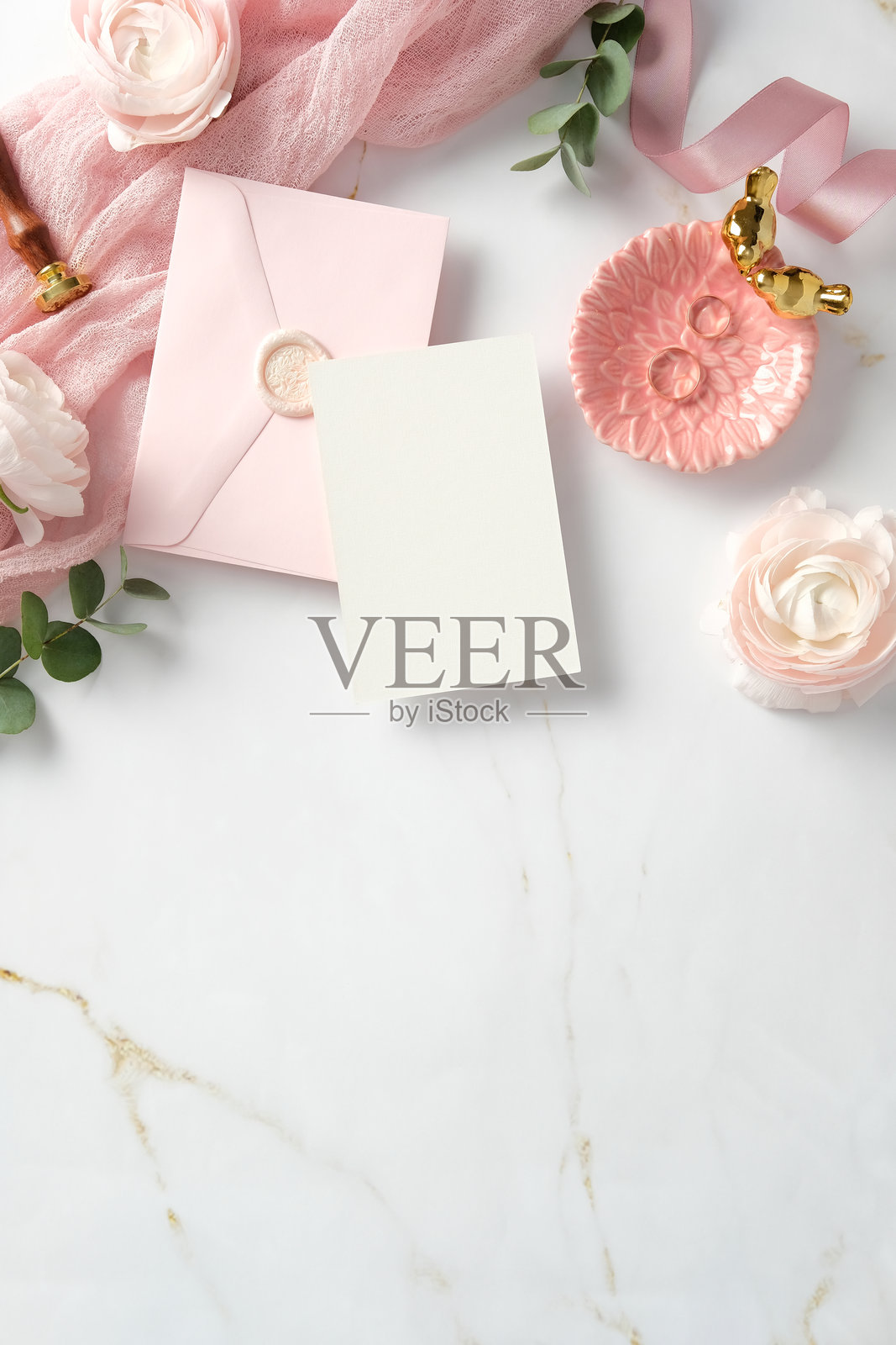 优雅的平铺图，展示了一张空白卡片和一个粉色信封，周围环绕着精致的花朵、蜡封和装饰元素，背景为大理石表面。非常适合婚礼邀请函或浪漫公告。照片摄影图片