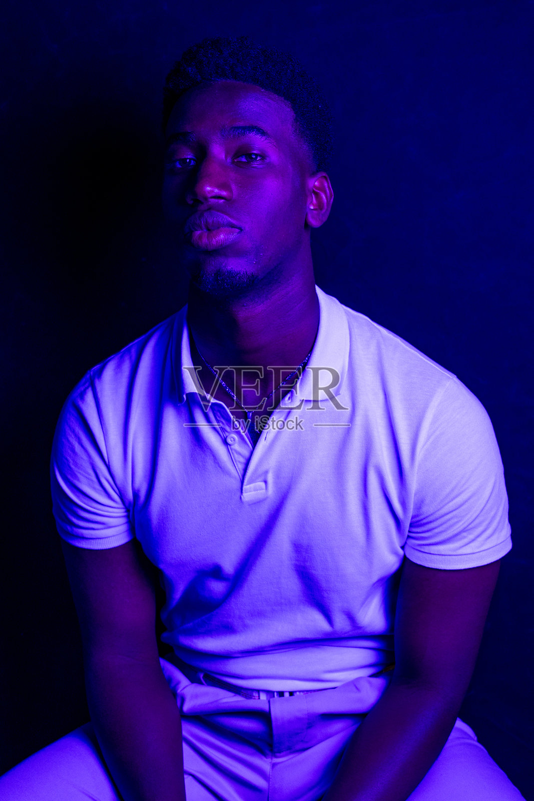 年轻男子在蓝光下摆姿势，穿着白色 polo 衫照片摄影图片