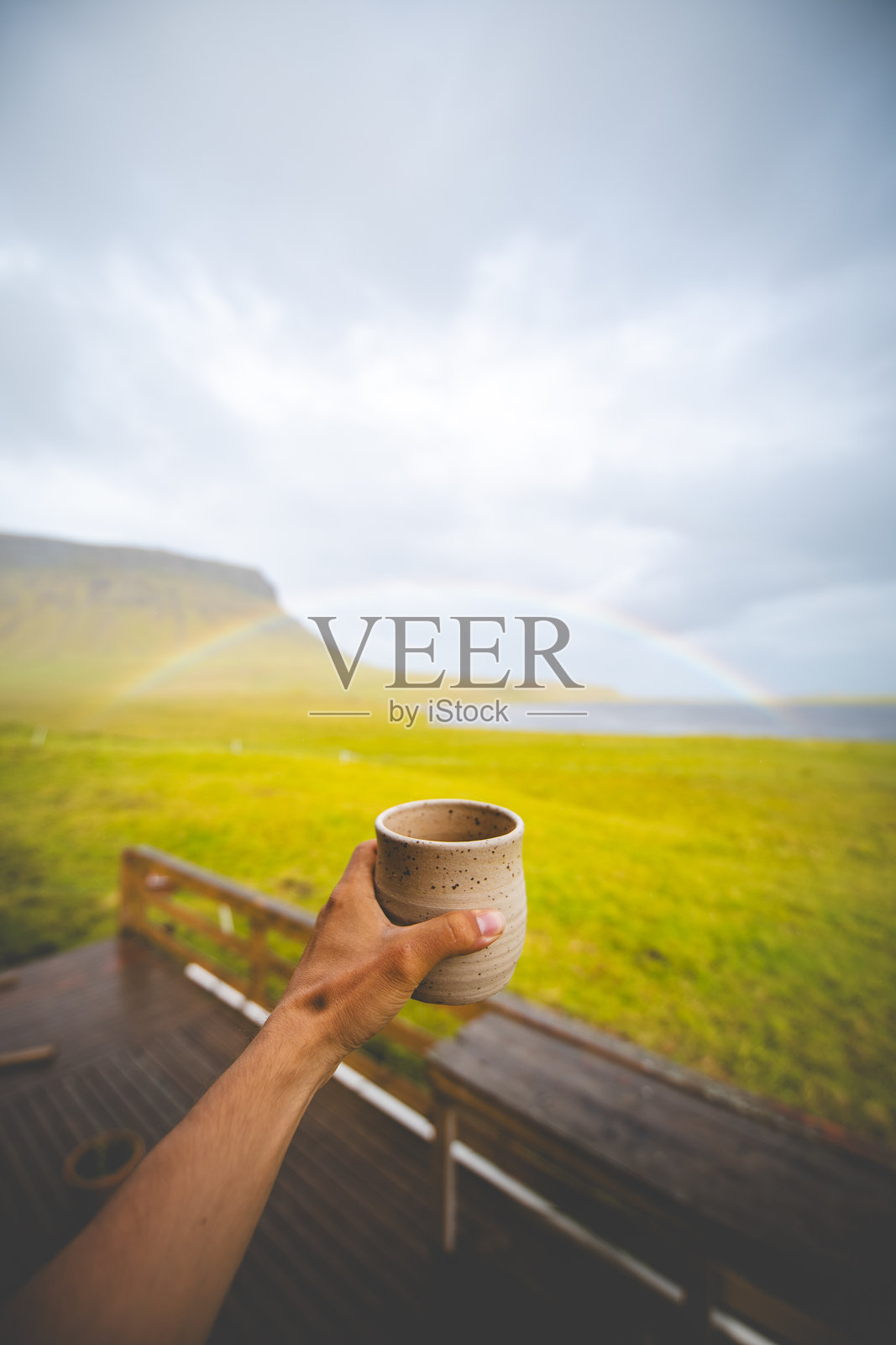 生动的彩虹横跨在宁静的冰岛草地上方的多云天空。冰岛西部的斯奈山半岛。鲜艳的色彩与柔和的阴郁云朵和金色草地形成了美丽的对比。照片摄影图片