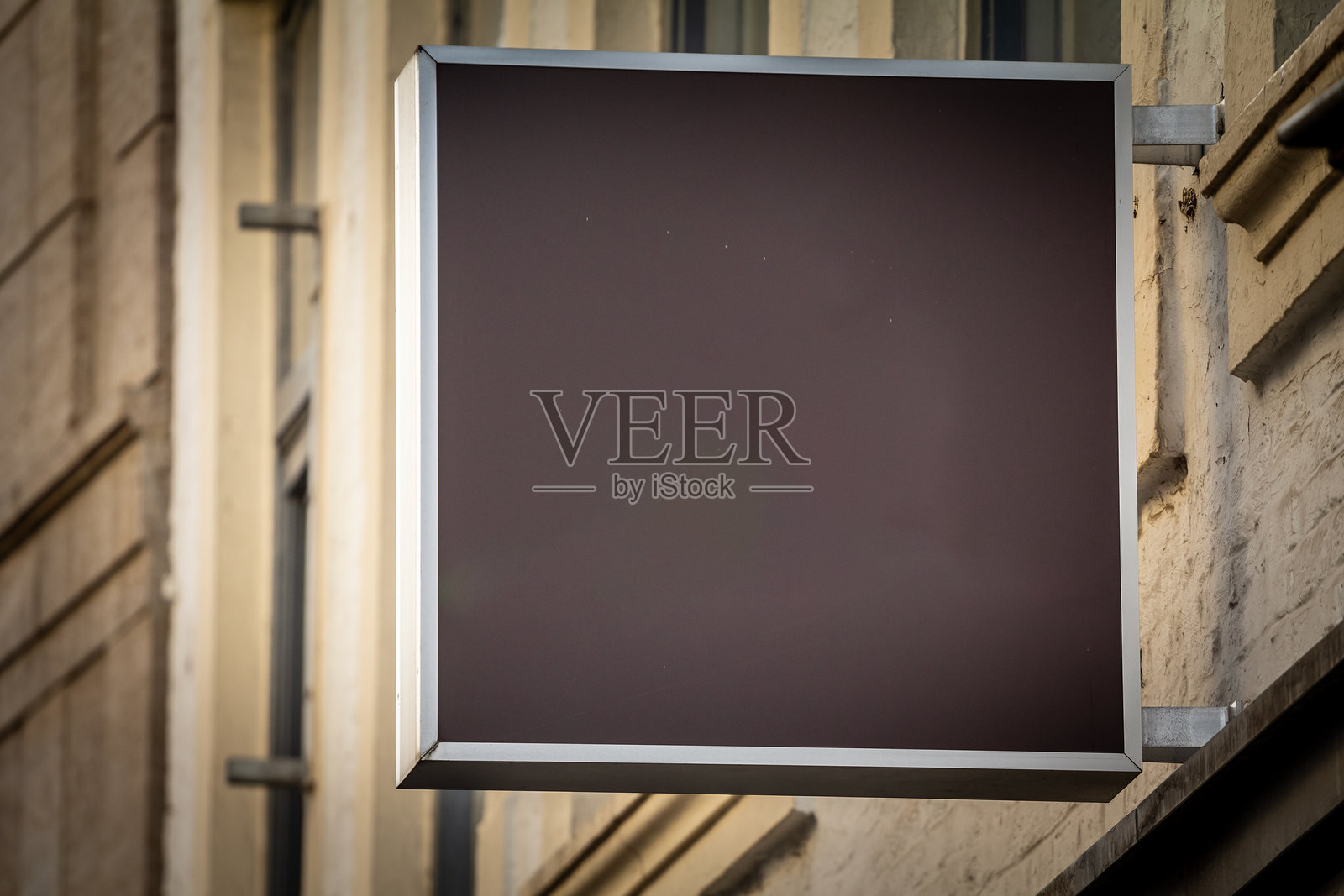 一块矩形黑色标牌在商店外空白地矗立，与建筑物的浅色外立面形成对比。这种简洁的设计为品牌标识或广告做好了准备。照片摄影图片