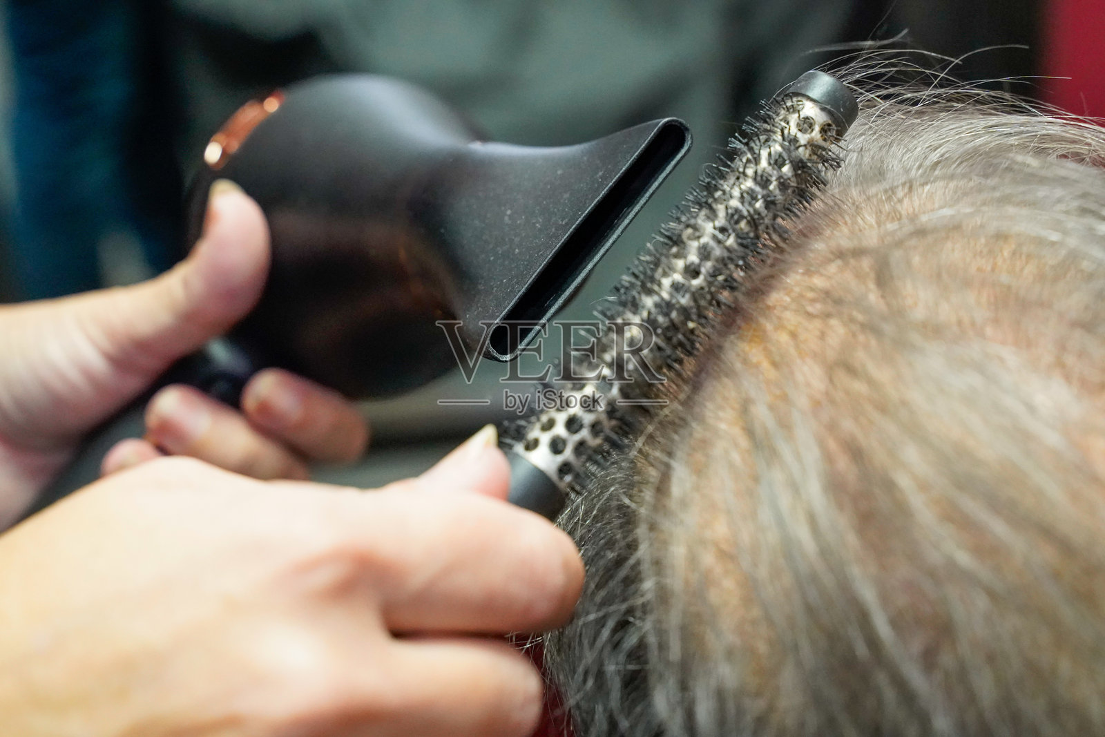 美容院里，发型师正在为一位女性吹干头发照片摄影图片