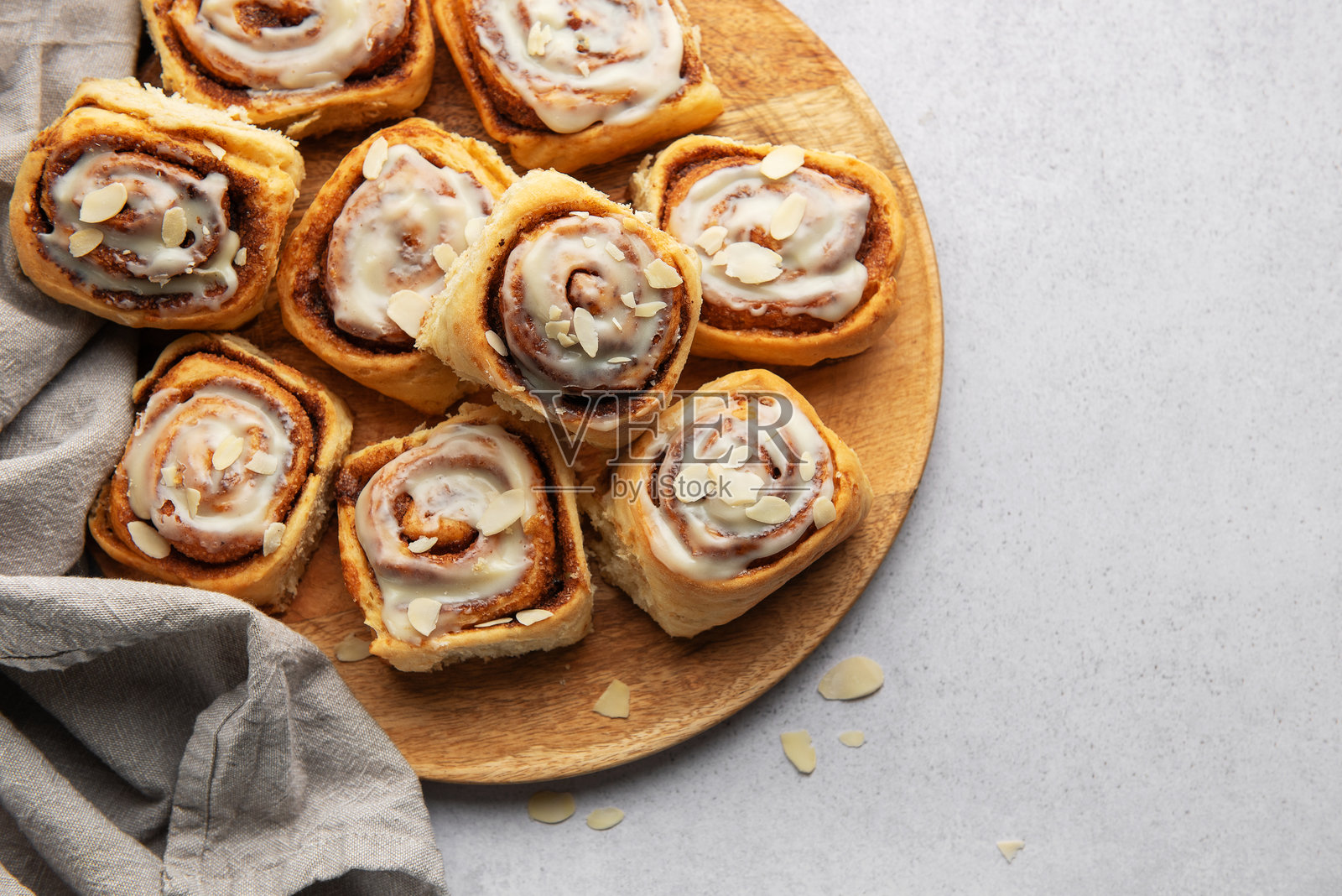 美味的肉桂卷上面有白色糖霜和杏仁片，静静地放在木盘上照片摄影图片