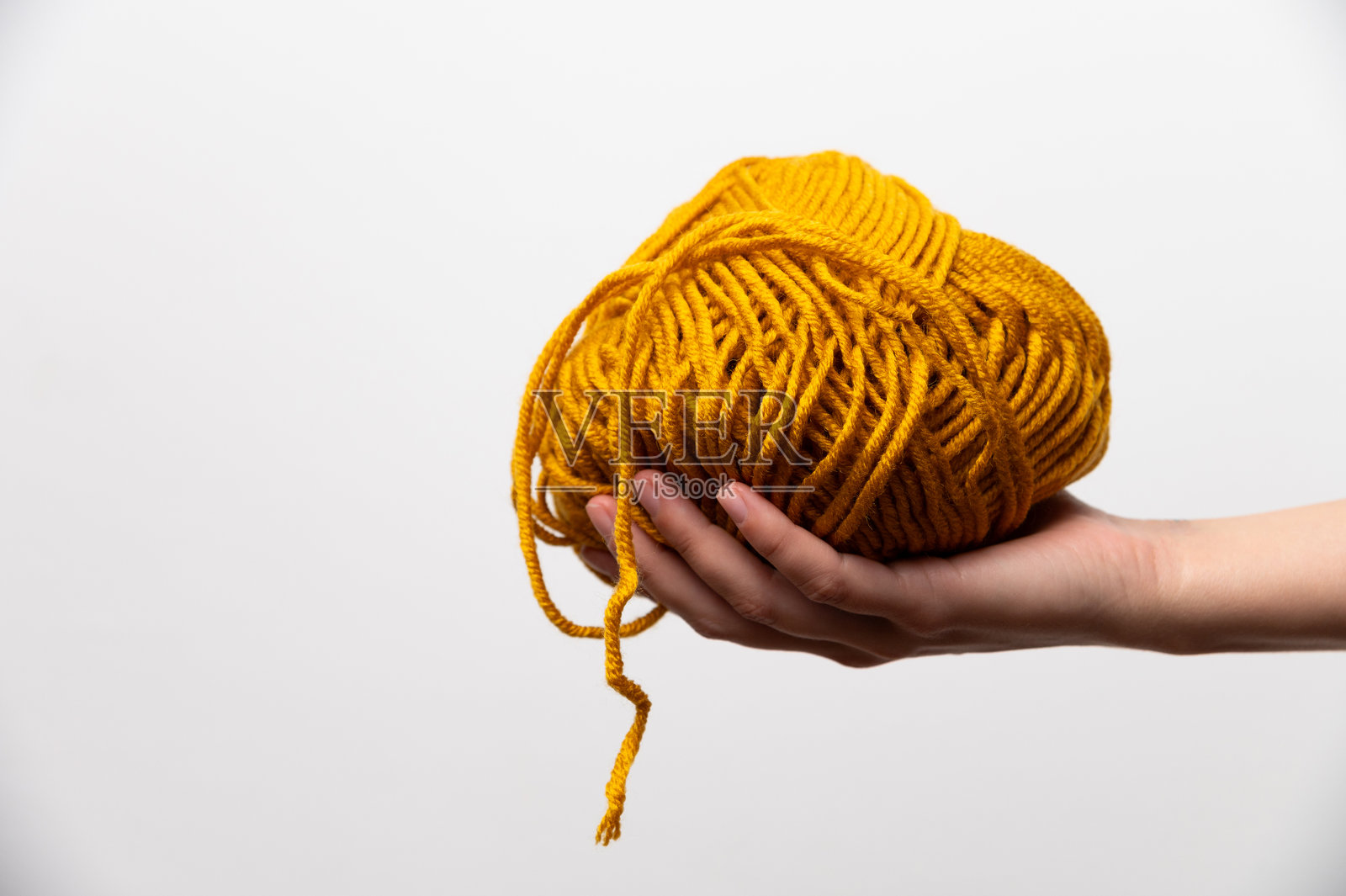 女性手侧面握着橙色毛线球，背景为白色照片摄影图片