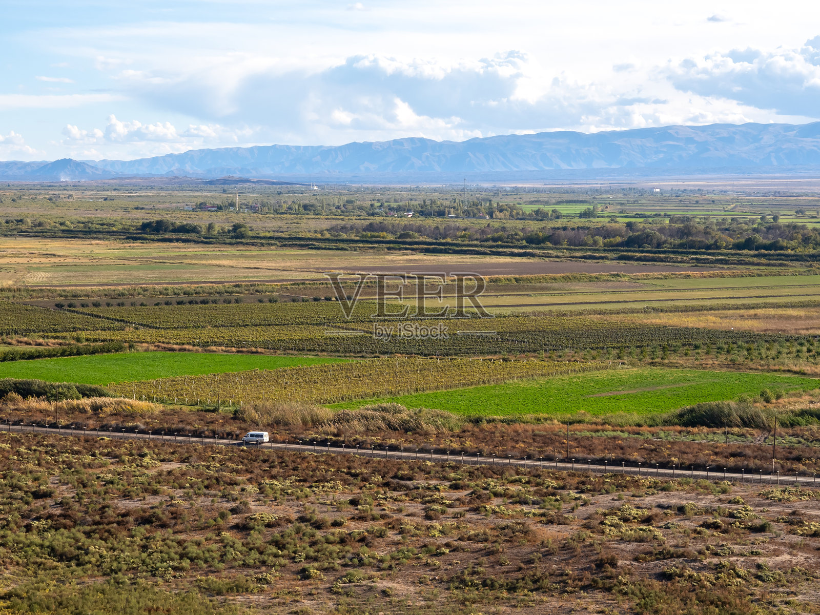 白色面包车在公路上，背景是美丽的农业农场和绿色田野，蓝天白云，视野开阔，位于靠近山脉的山丘上。照片摄影图片
