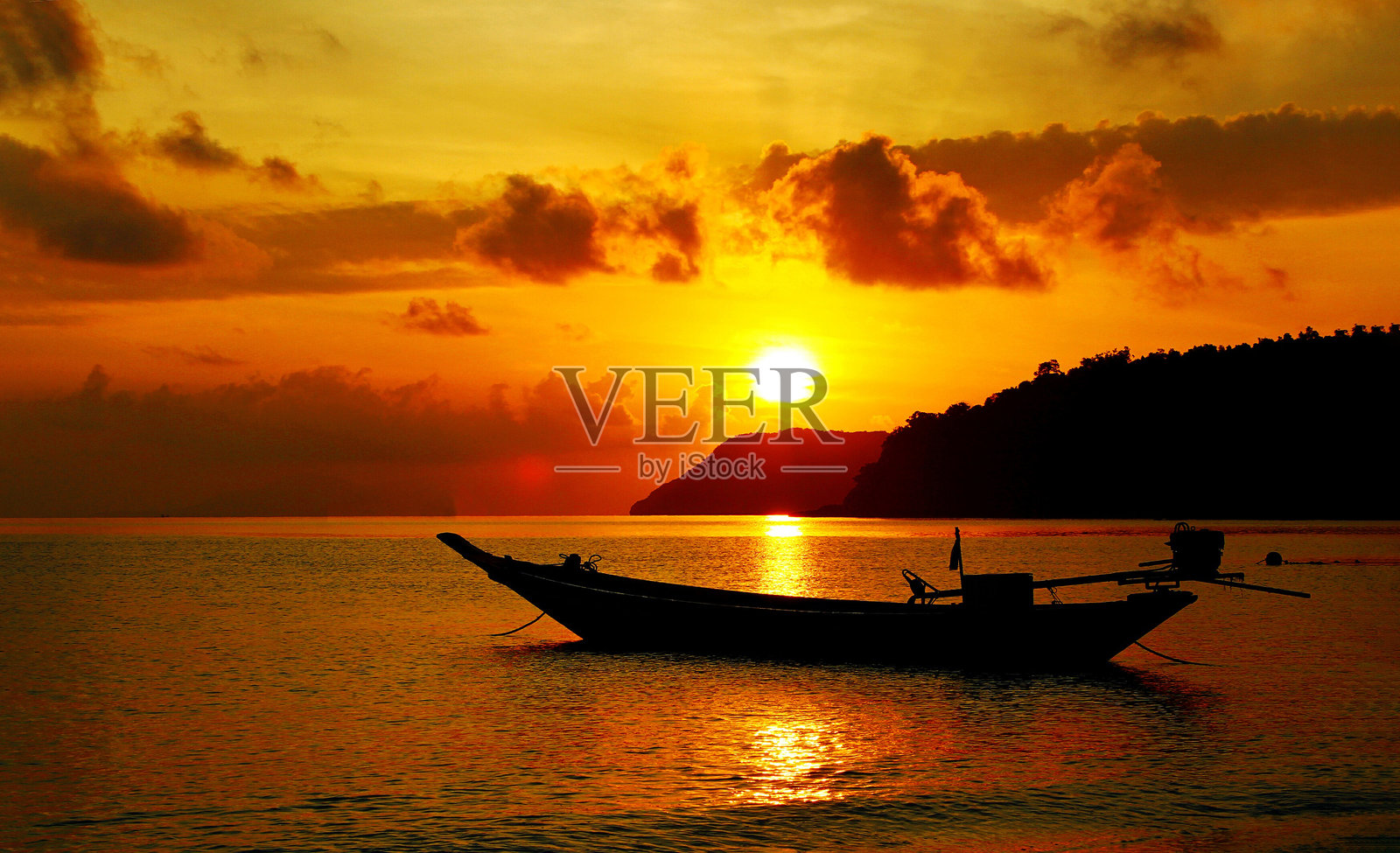 清晨，长尾船停泊在橙色天空、云山和日出背景的海面上的剪影。照片摄影图片