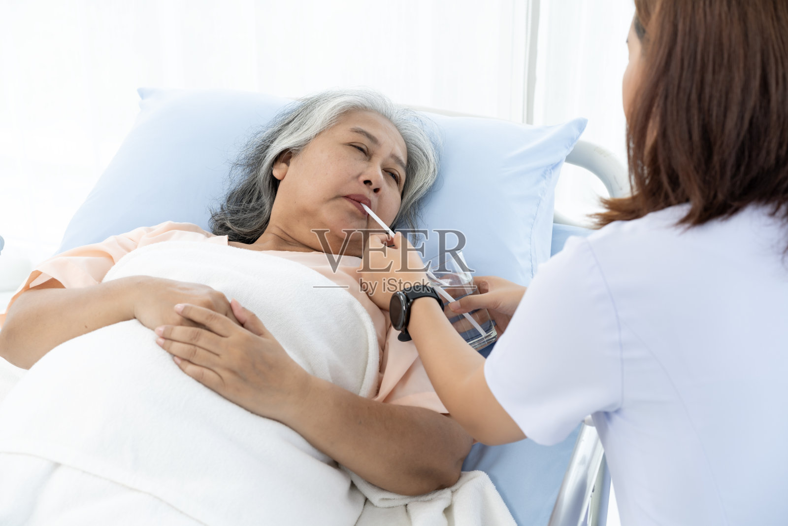 护士把水放进杯子里，用吸管喂给她喝。照片摄影图片