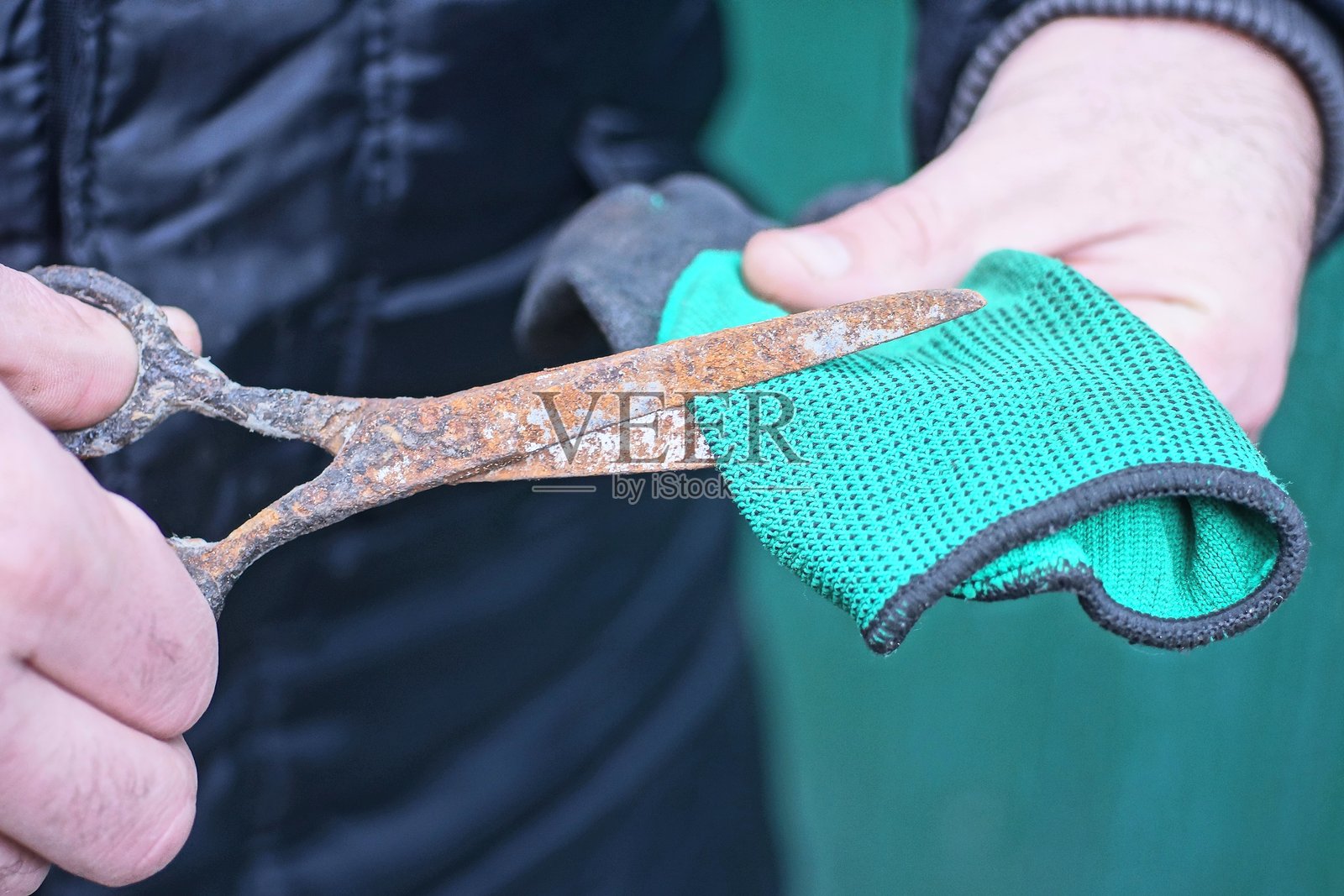 男性工人手持生锈的棕色铁剪刀剪裁绿色布料照片摄影图片