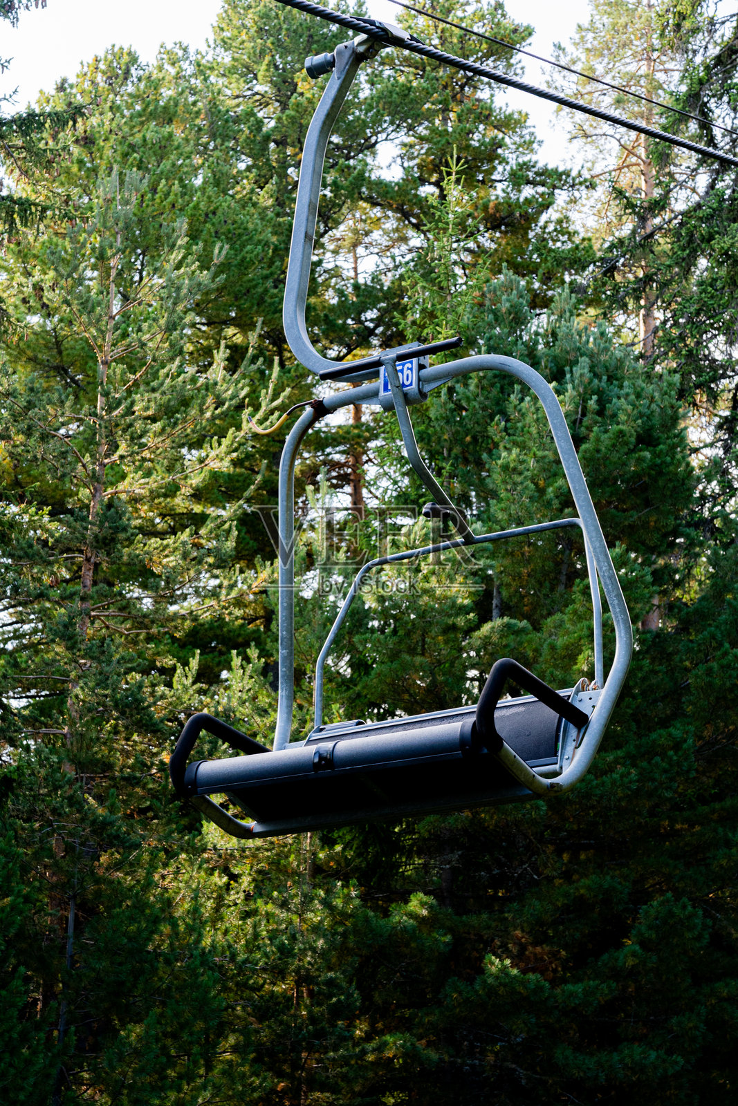 山顶缆车悬浮在郁郁葱葱的森林树冠上，悬挂在电缆上，背景是清澈的蓝色夏日天空和原始的自然风光。照片摄影图片