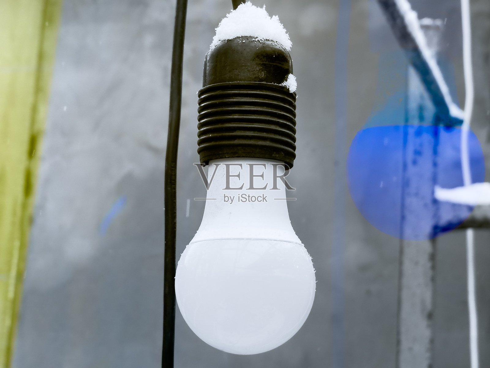 一盏被雪覆盖的灯泡悬挂在电线上，展现了一个寒冷的冬日，色调柔和，氛围冰冷。照片摄影图片