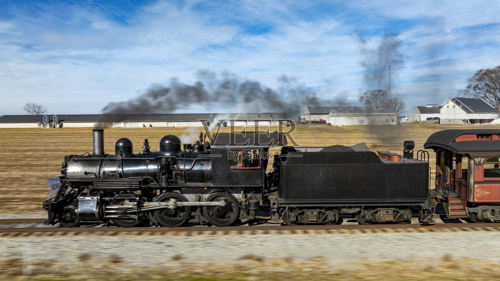 历史蒸汽机车在晴朗的日子里穿过开阔的田野和农舍，缓缓前行。照片摄影图片